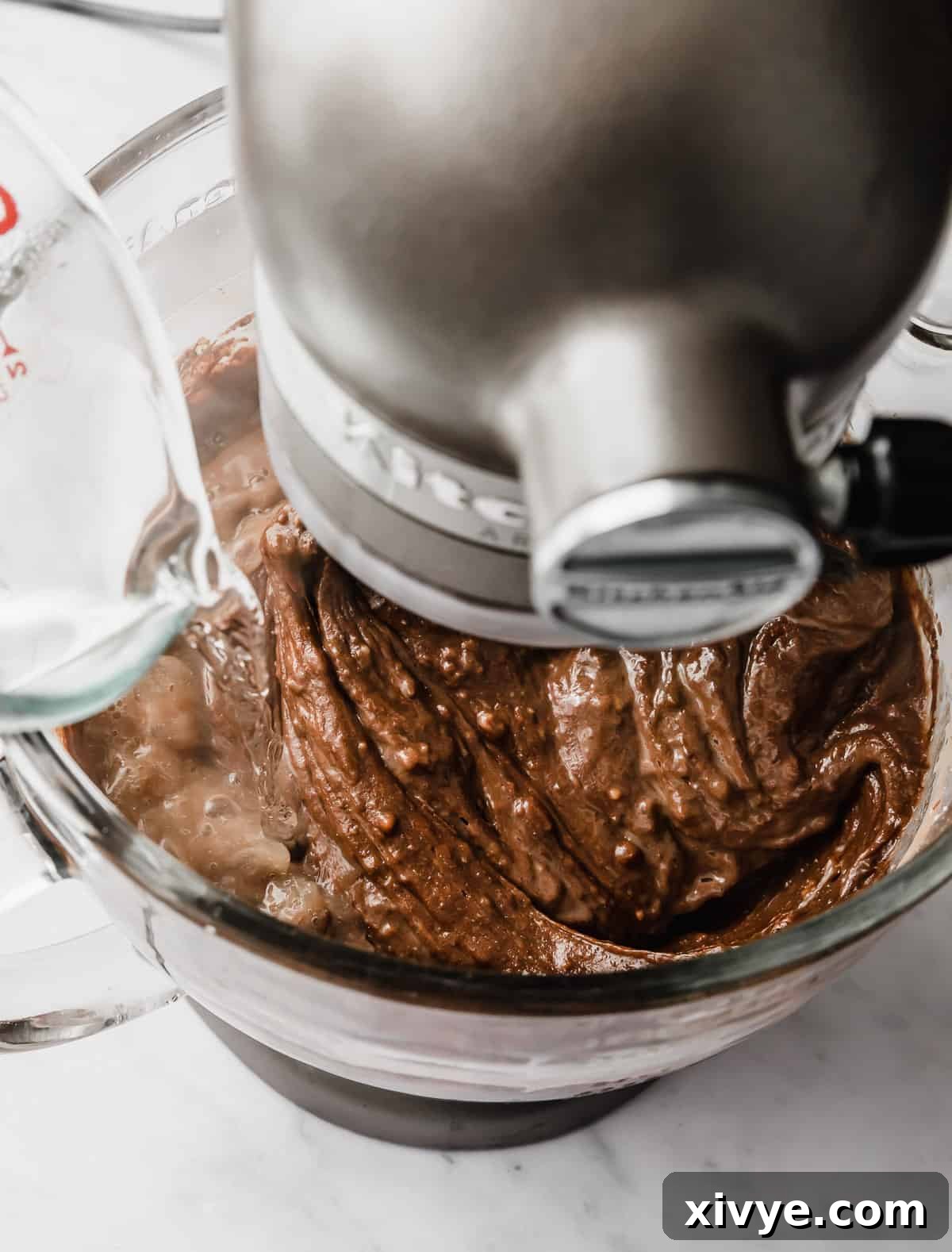 Hot water being poured into a glass bowl filled with a chocolate Bundt Cake batter.