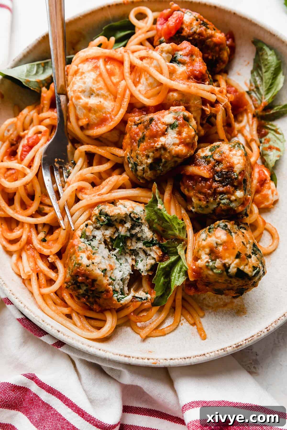 A close up photo of succulent turkey spinach meatballs nestled atop al dente spaghetti noodles, generously coated in marinara sauce.