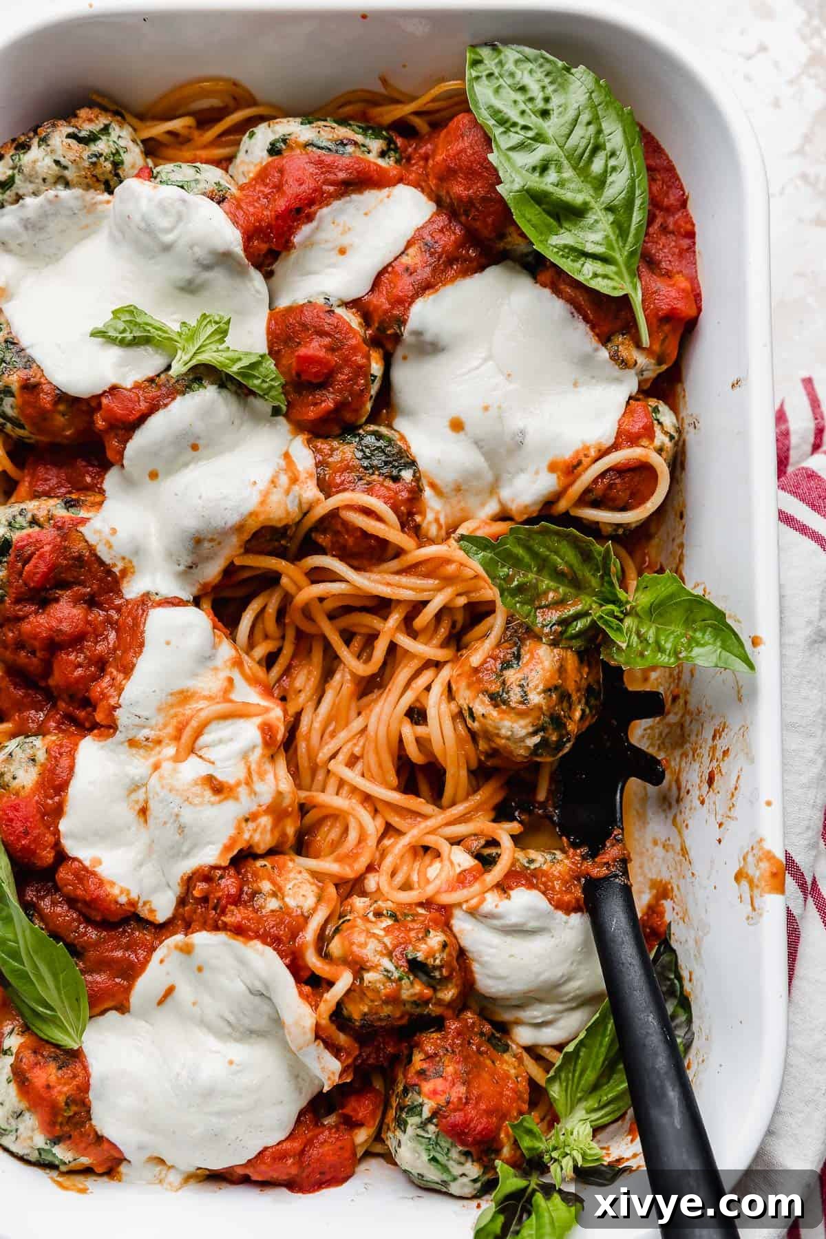 A pristine white baking dish showcasing marinara-coated spaghetti noodles elegantly topped with juicy turkey spinach meatballs and glistening melted mozzarella cheese.