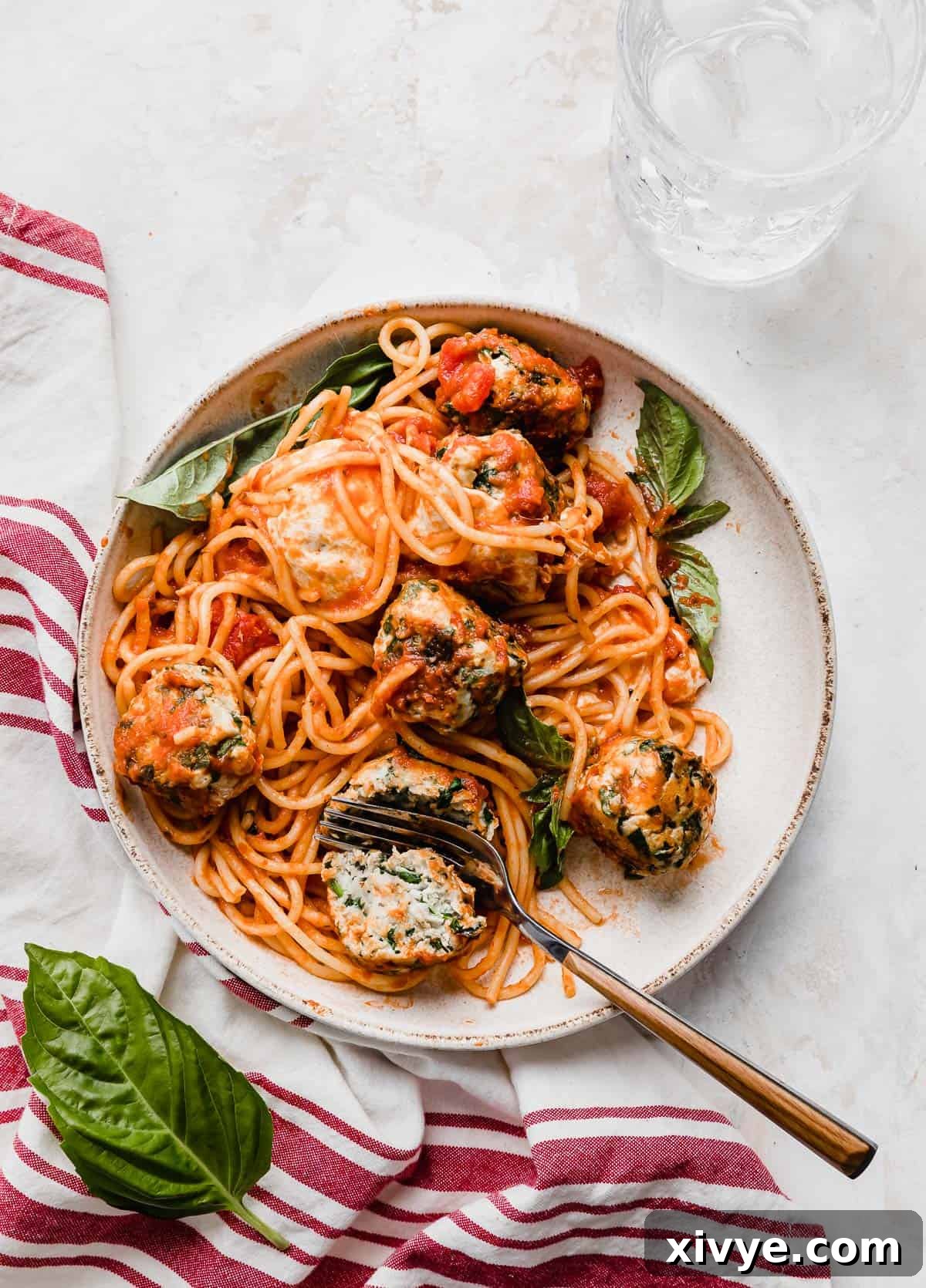 A perfectly plated dish of Turkey Spinach Meatballs and Spaghetti on a white plate, accompanied by a charming red striped towel on the side, ready to be enjoyed.