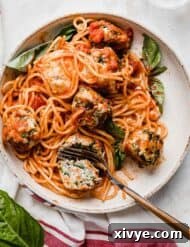 Marinara coated spaghetti noodles on a white plate topped with turkey spinach meatballs.