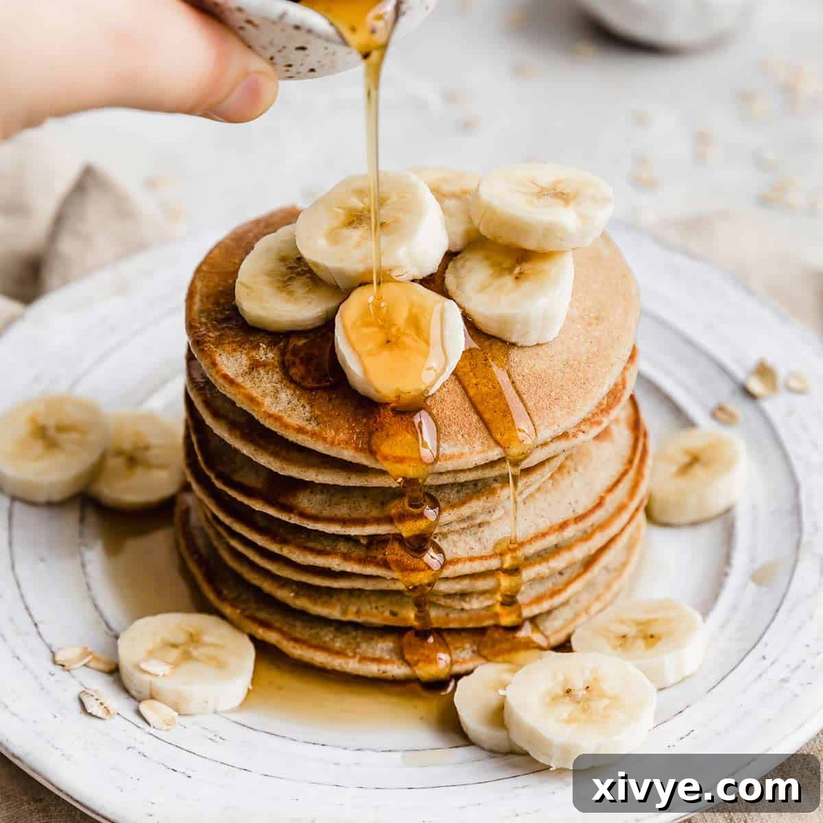 A stack of Banana Oatmeal Pancakes topped with sliced bananas.