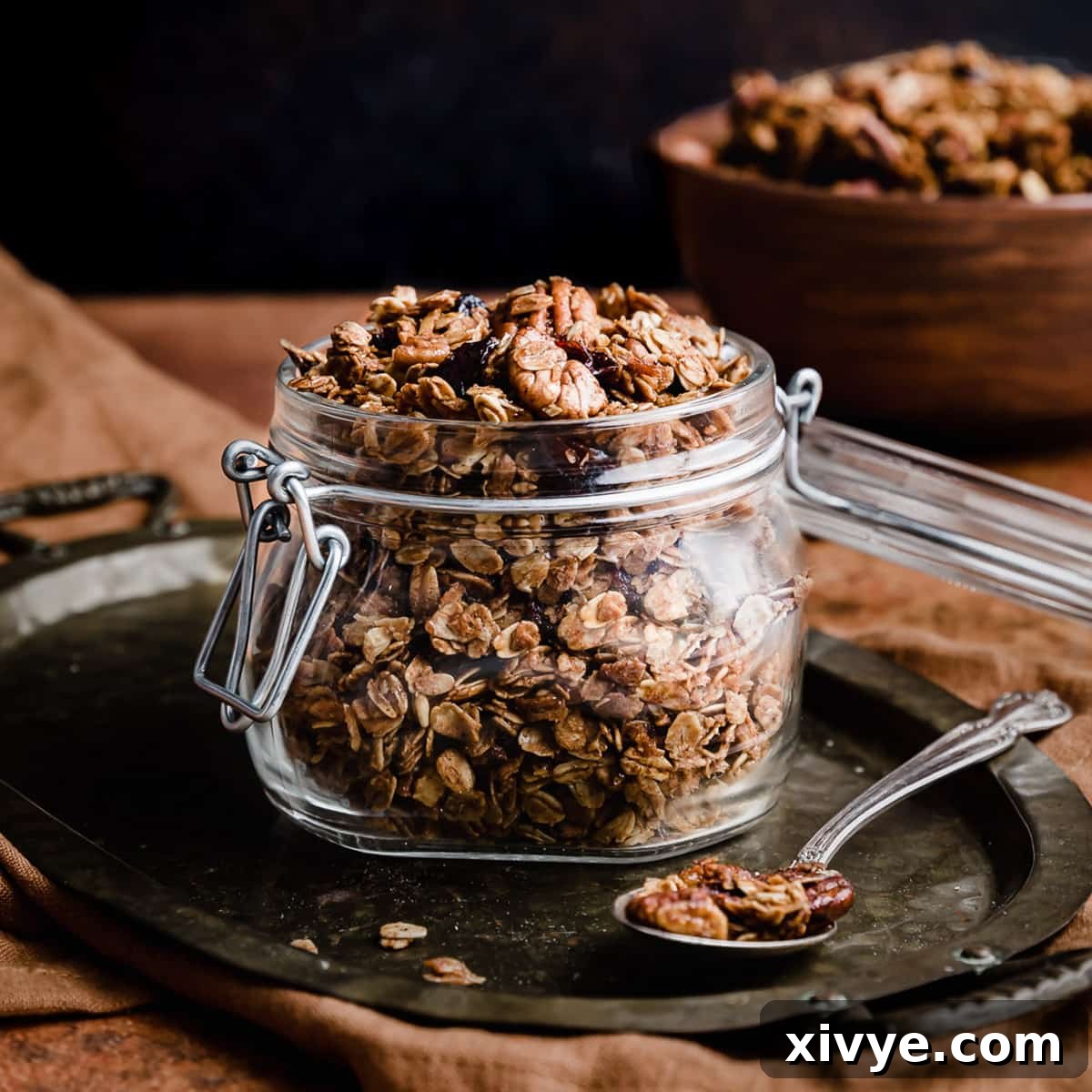 Gingerbread Granola in a glass jar against a black background.