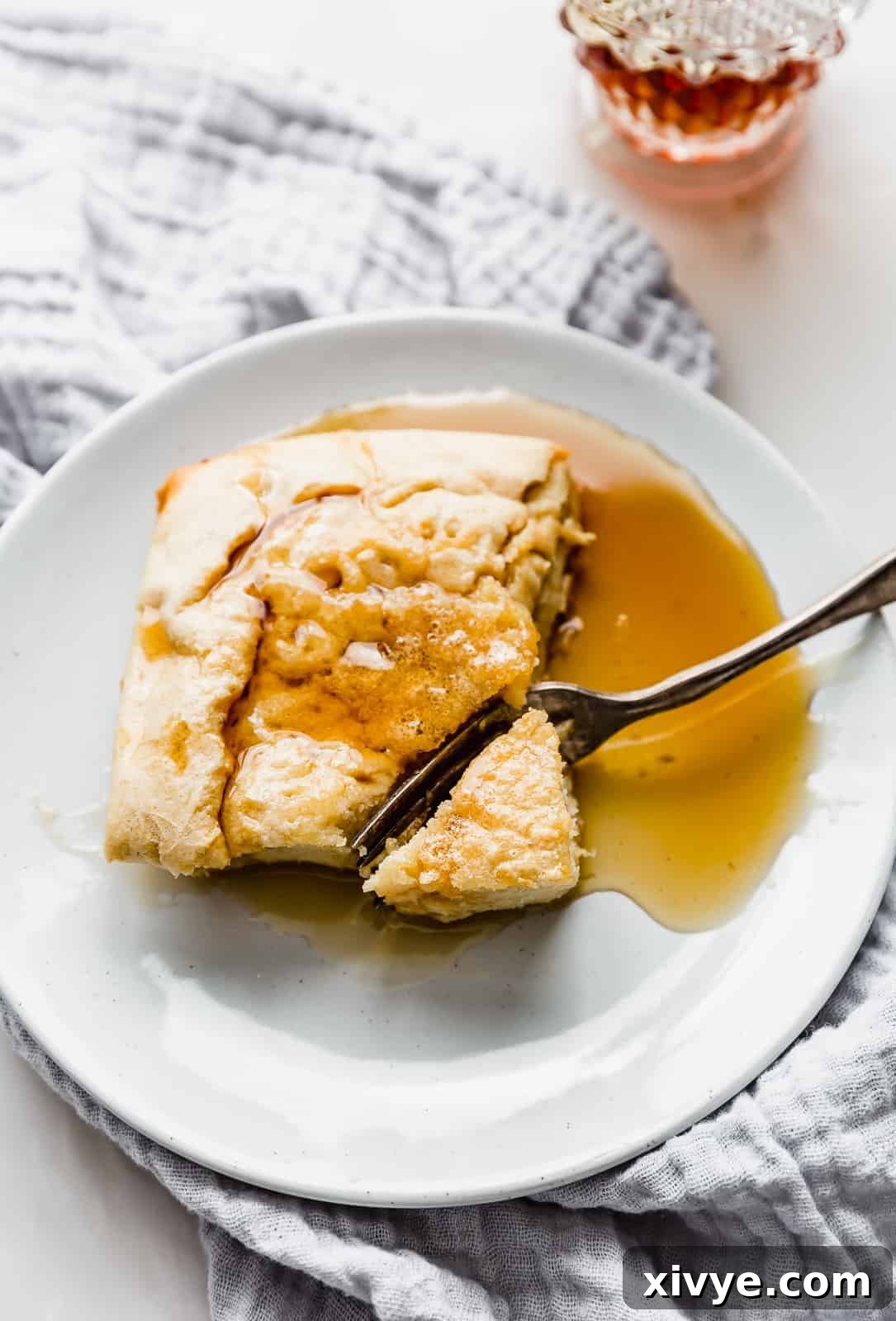 A square slice of German pancake on a white plate topped with syrup.