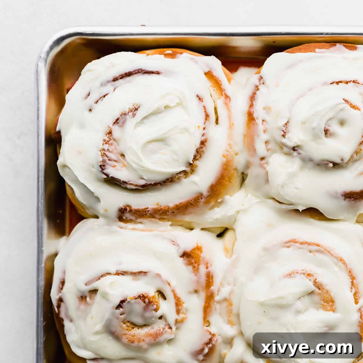 White frosting covered Orange Rolls on a baking sheet.