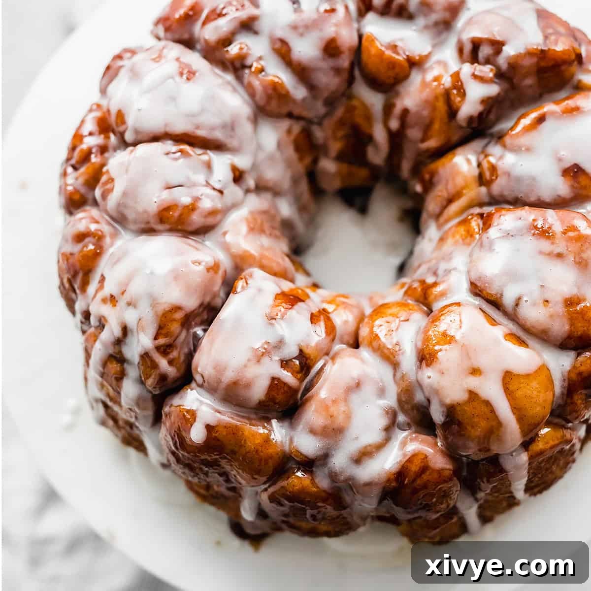 The Best Monkey Bread Recipe covered in a white glaze on a white plate.