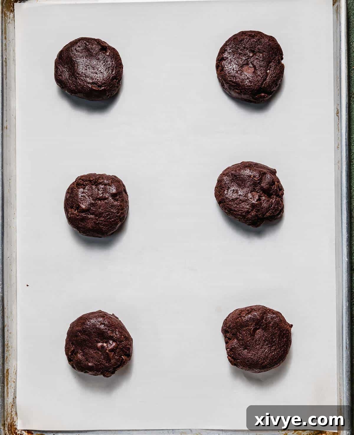 Peppermint Bark Bites 5 Six chocolate cookie dough balls on a white parchment lined baking sheet.
