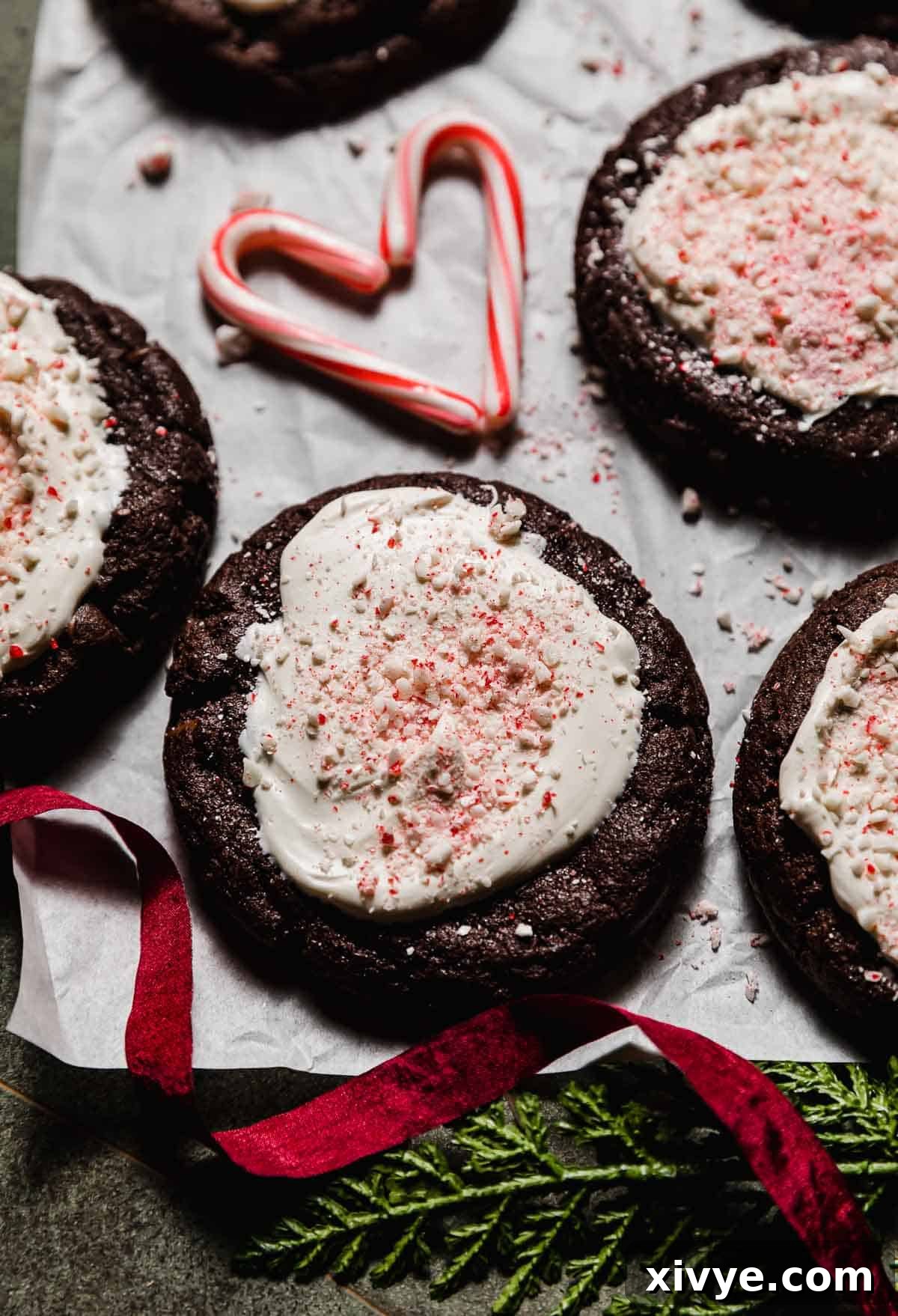 Peppermint Bark Bites 8 Chocolate cookie topped with white chocolate and crushed candy canes (Peppermint Bark Cookie) on a white parchment paper with a small candy cane heart in the background.