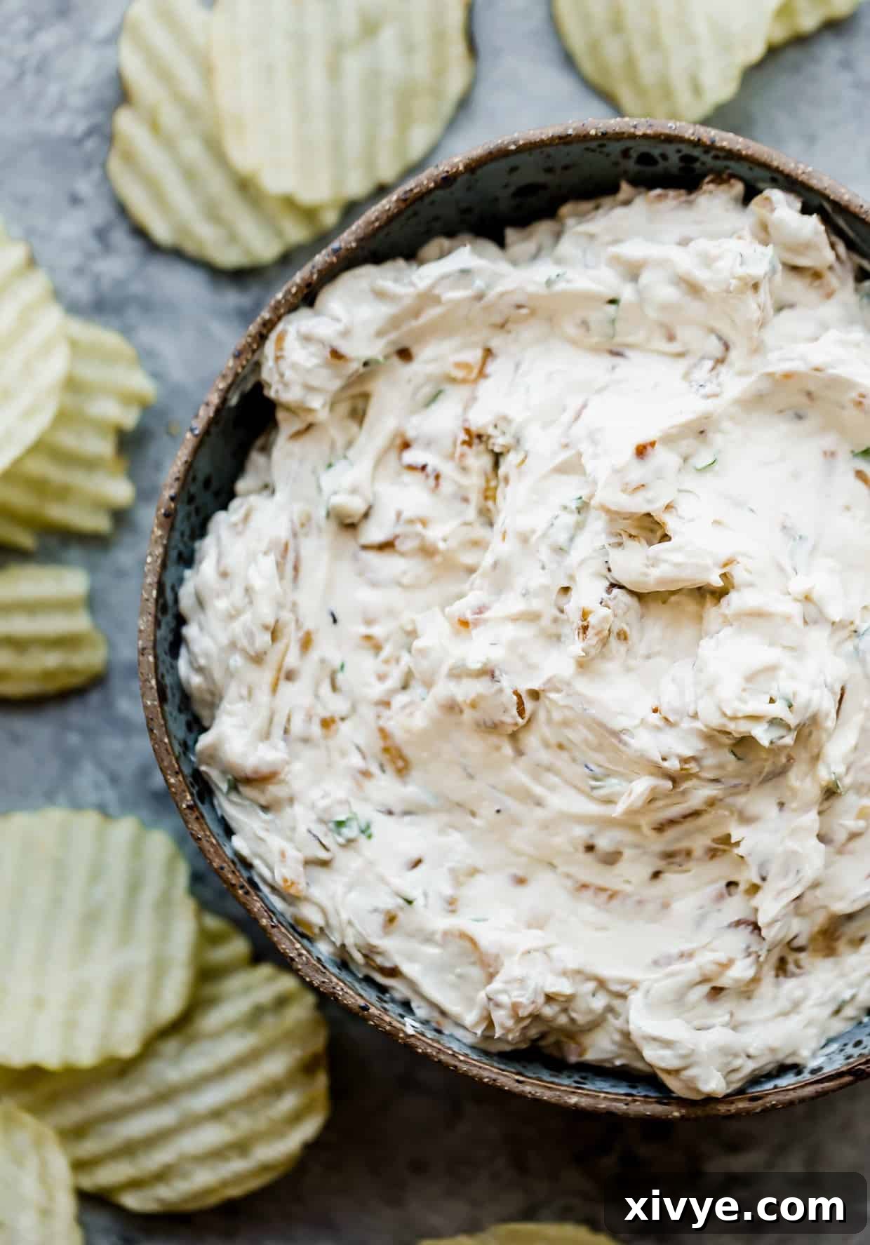 Velvety Onion Cream Cheese Dip 2 Onion dip in a bowl with ruffled potato chips around the bowl.