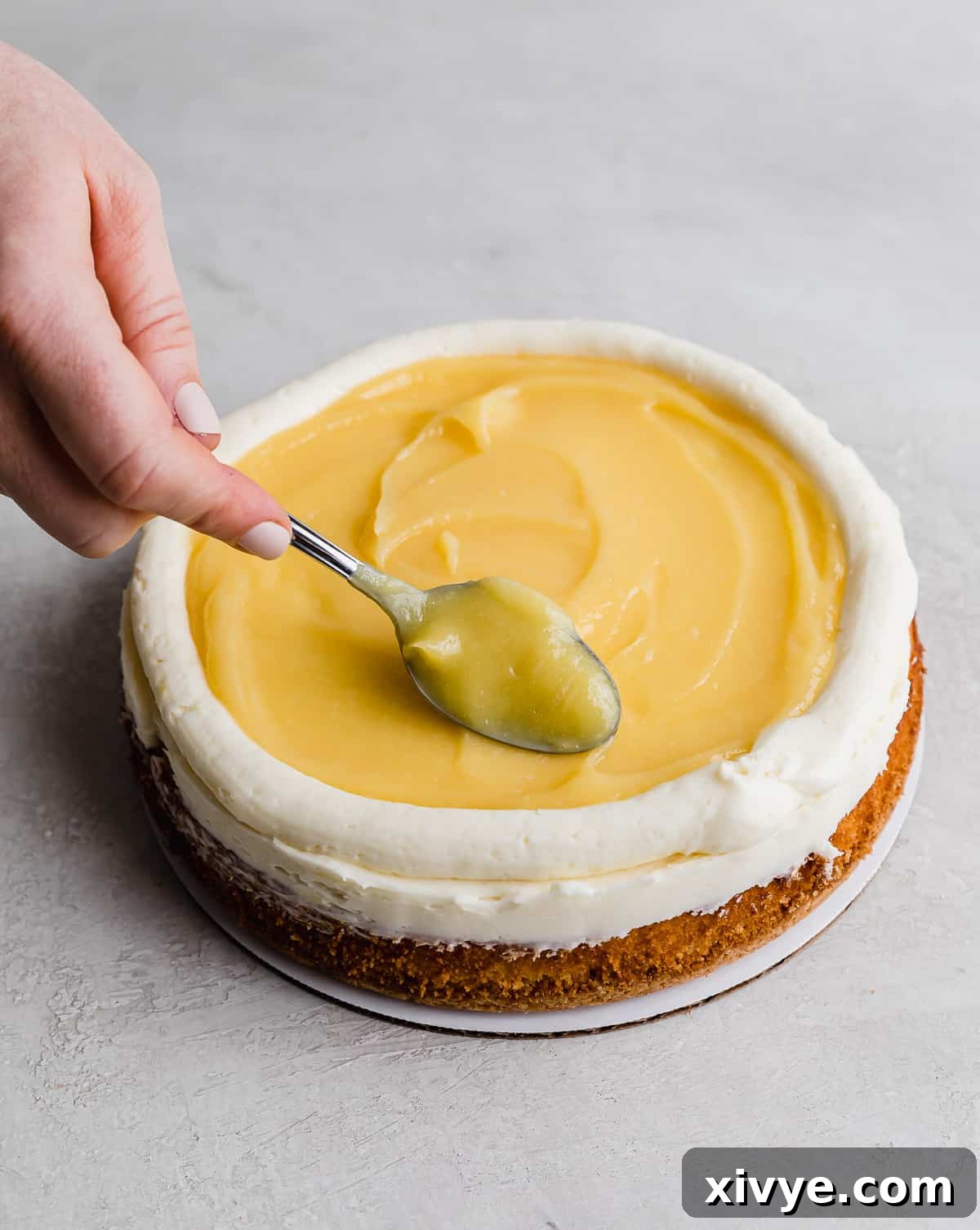 A spoon swirling the lemon curd on top of a Lemon Bar Cake for a decorative finish.