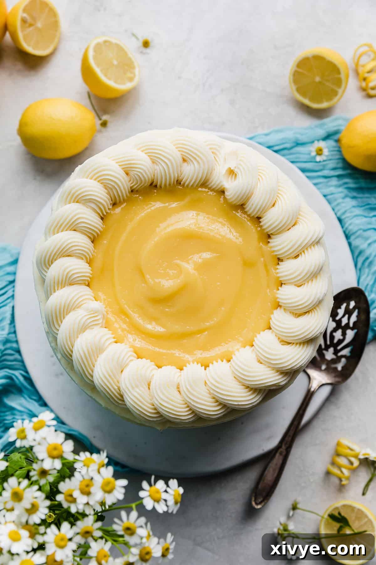 Overhead photo of a whole Lemon Bar Cake that's beautifully topped with a swirl of yellow lemon curd and a piped buttercream border.