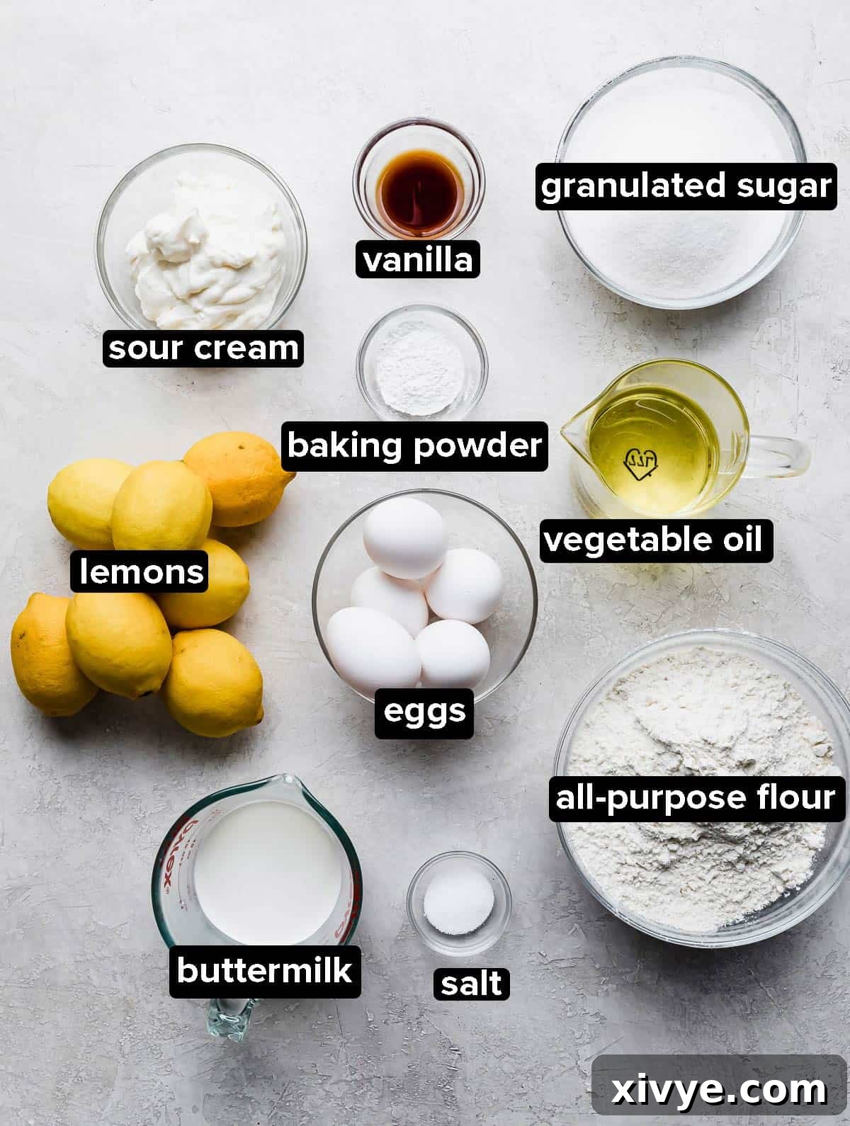 Lemon Bar Cake ingredients in glass bowls on a gray background, clearly laid out.