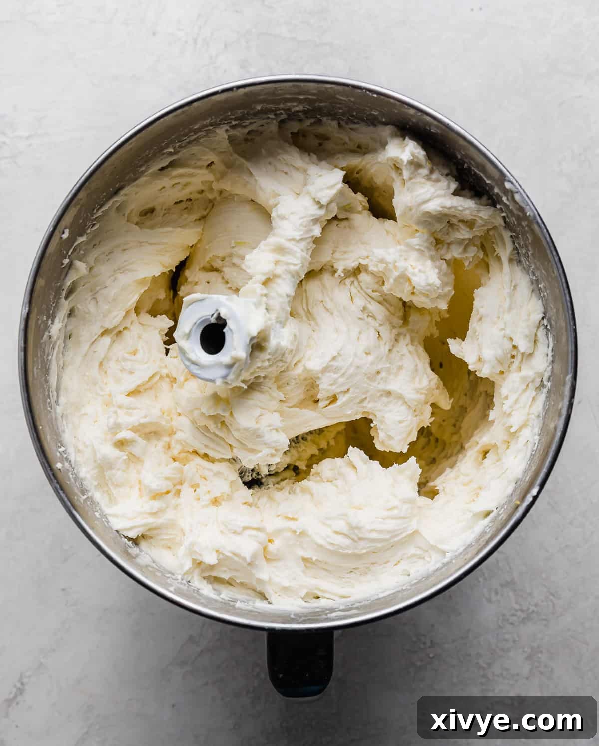 A silver mixing bowl filled with a luscious, white lemon buttercream frosting, ready for piping.