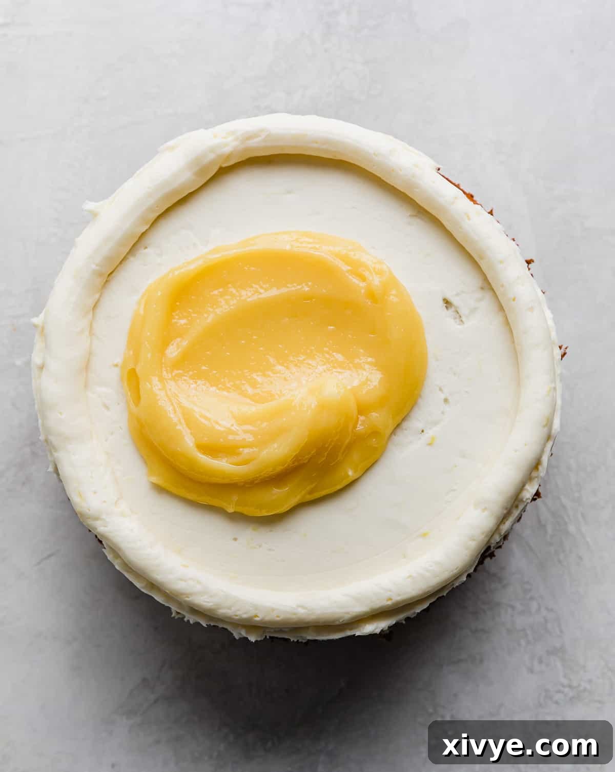 A dollop of bright yellow lemon curd being added on top of a buttercream frosted cake layer.