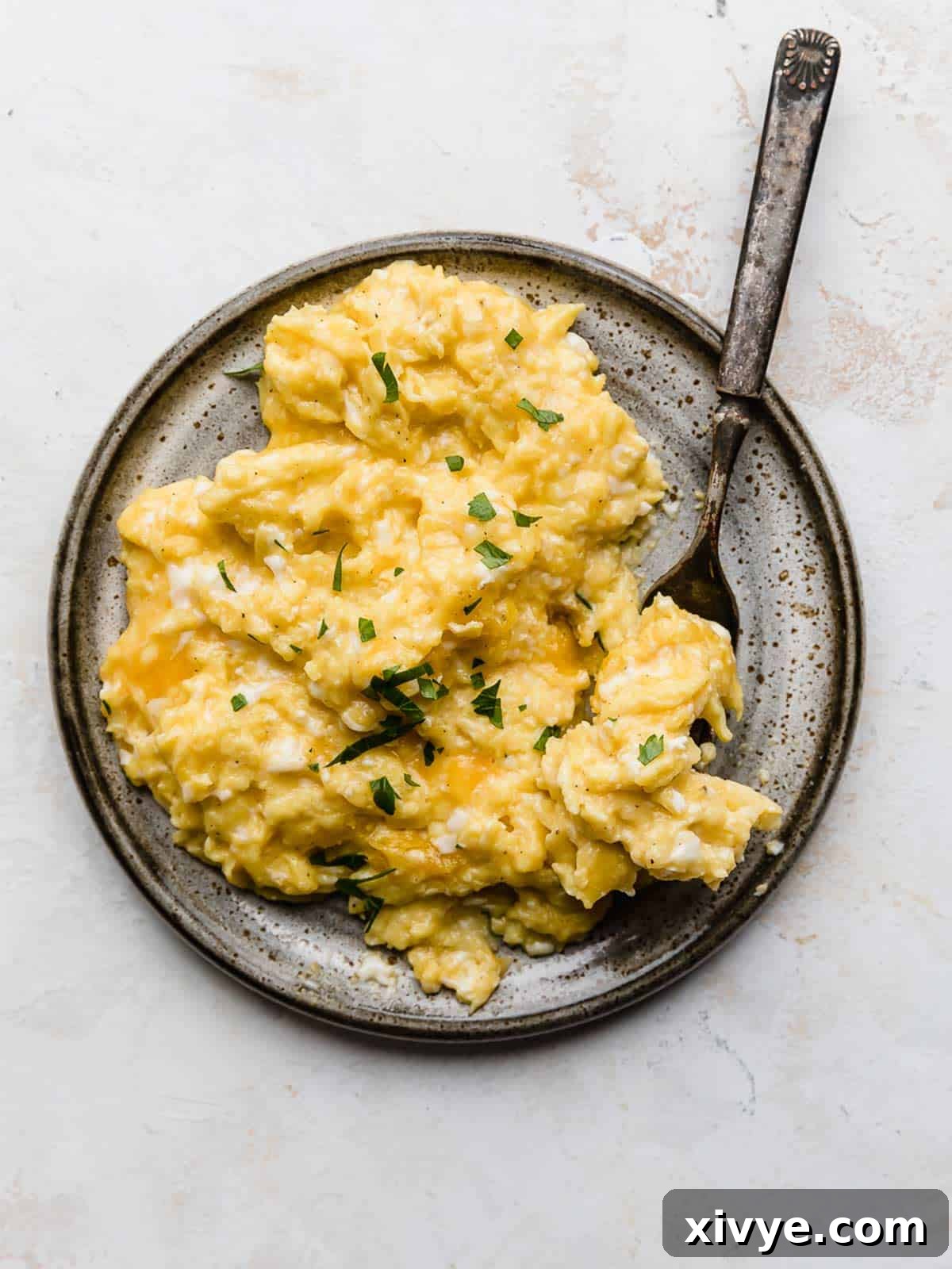 A beautifully plated dish of fluffy Cheesy Scrambled Eggs, generously garnished with fresh green parsley, inviting you to enjoy a perfect breakfast.