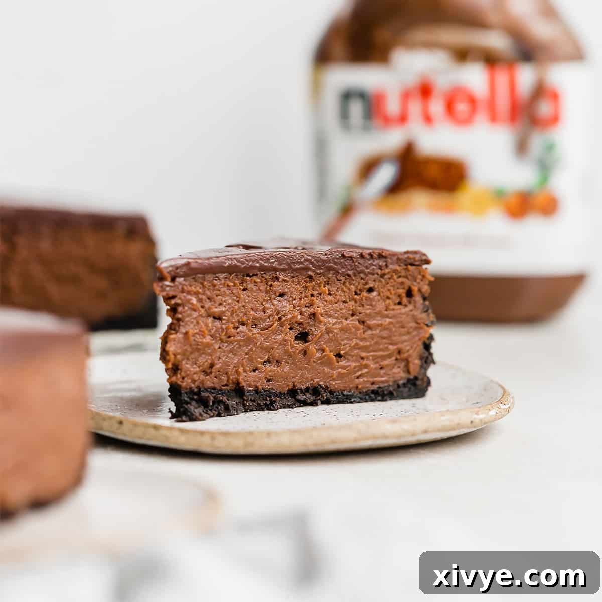 Irresistible Oreo Creations 25 A luscious slice of Nutella Cheesecake served on a plate, with a jar of Nutella subtly blurred in the background, inviting you to indulge.