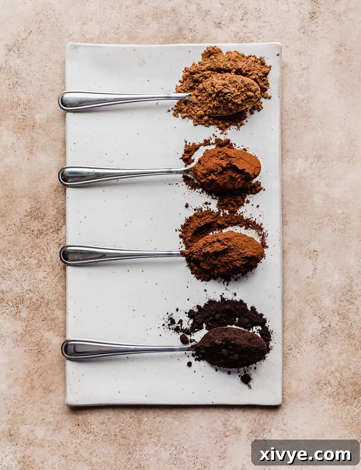 Four cocoa powders on separate spoons on a rectangular white plate.