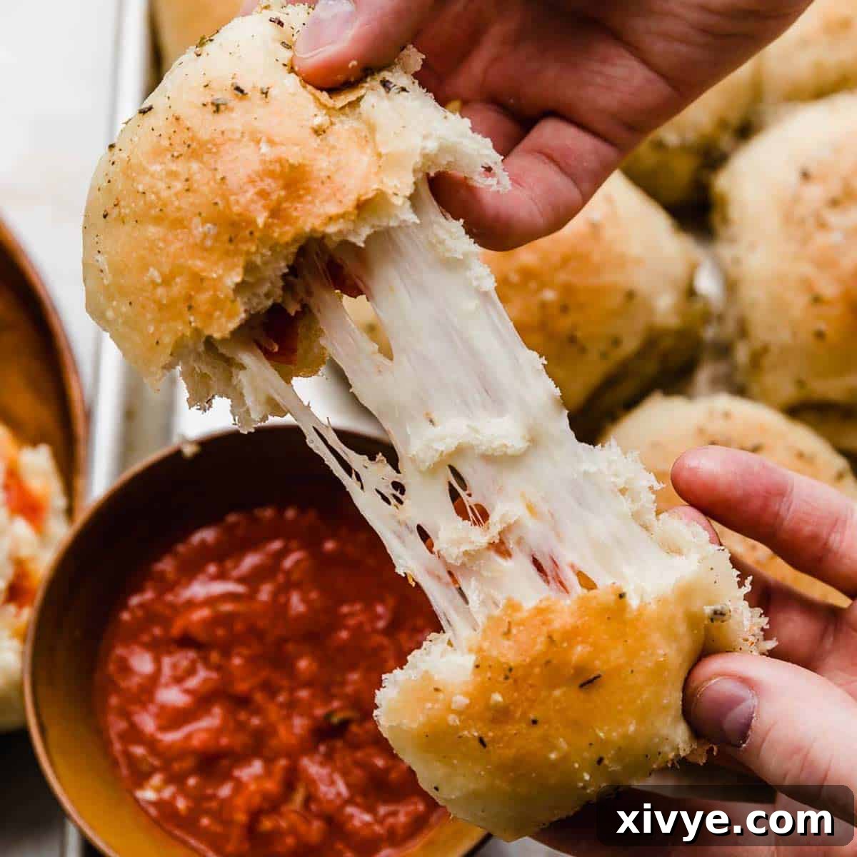Two hands gently pulling a hot pizza roll apart, revealing the deliciously stretchy mozzarella cheese and savory pepperoni melting inside.