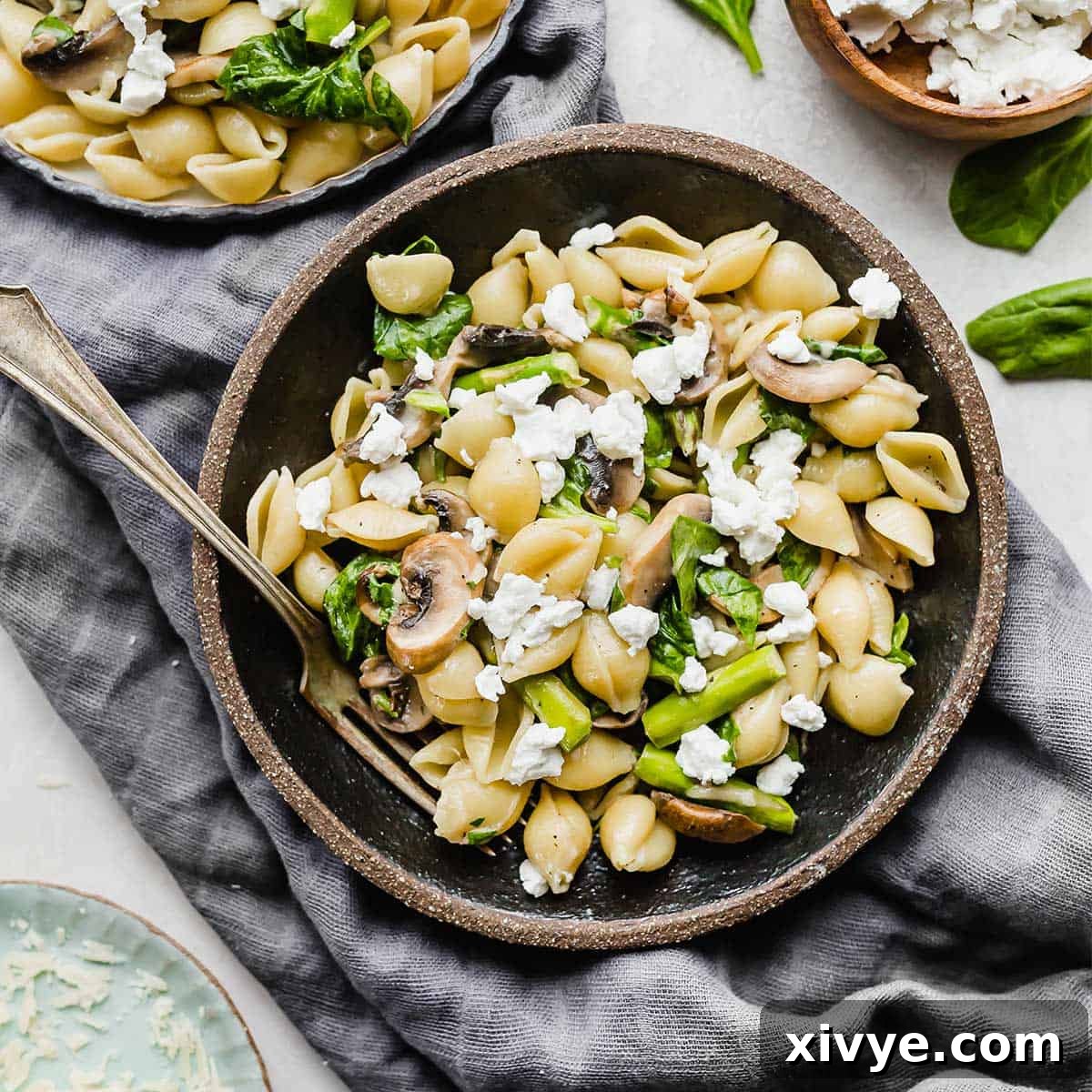 Asparagus Spinach Pasta, served in a sleek black bowl, resting on a dark gray linen napkin, beautifully garnished with crumbled goat cheese.