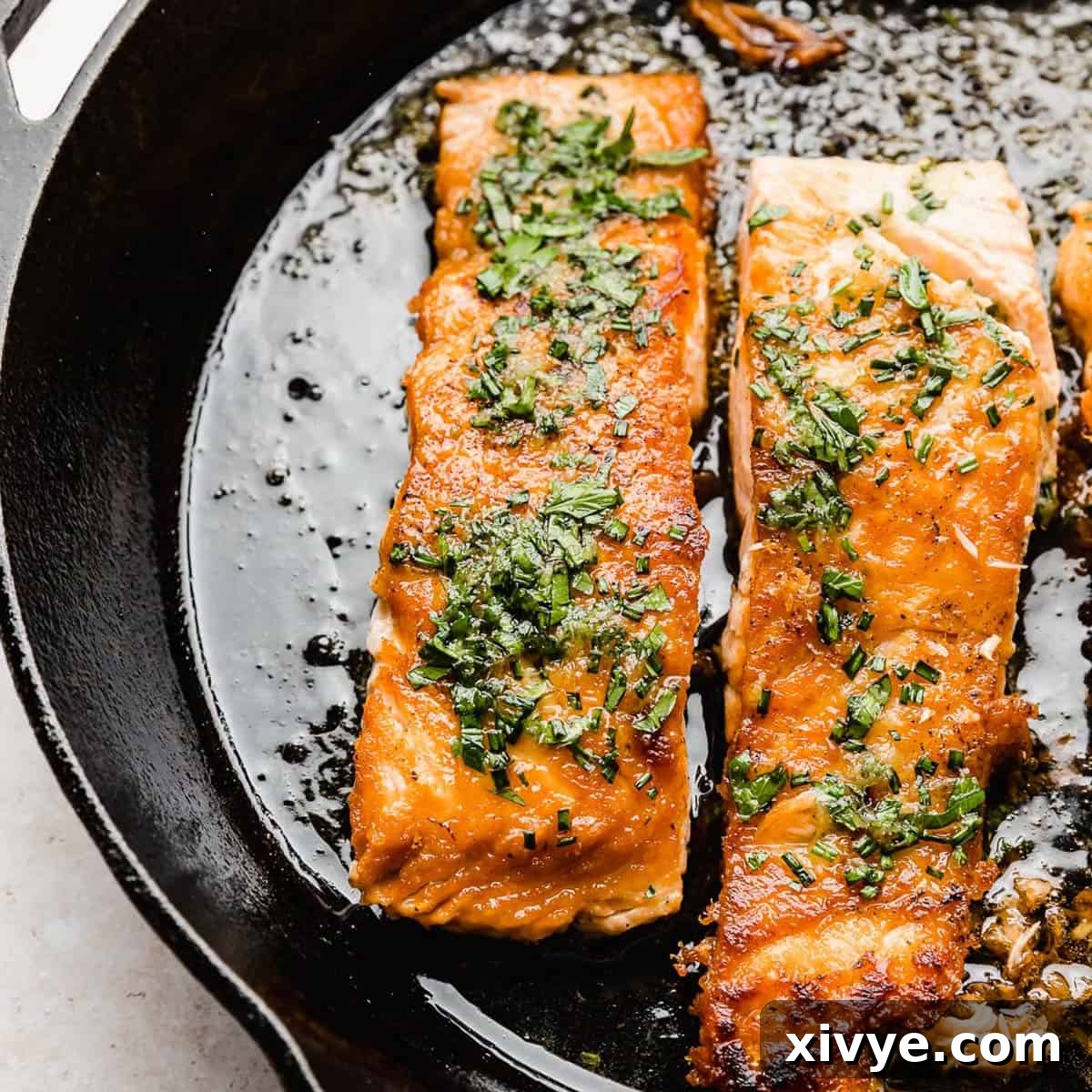 Beautifully seared Lemon Honey Glazed Salmon, glistening in a dark black skillet, ready to be served.