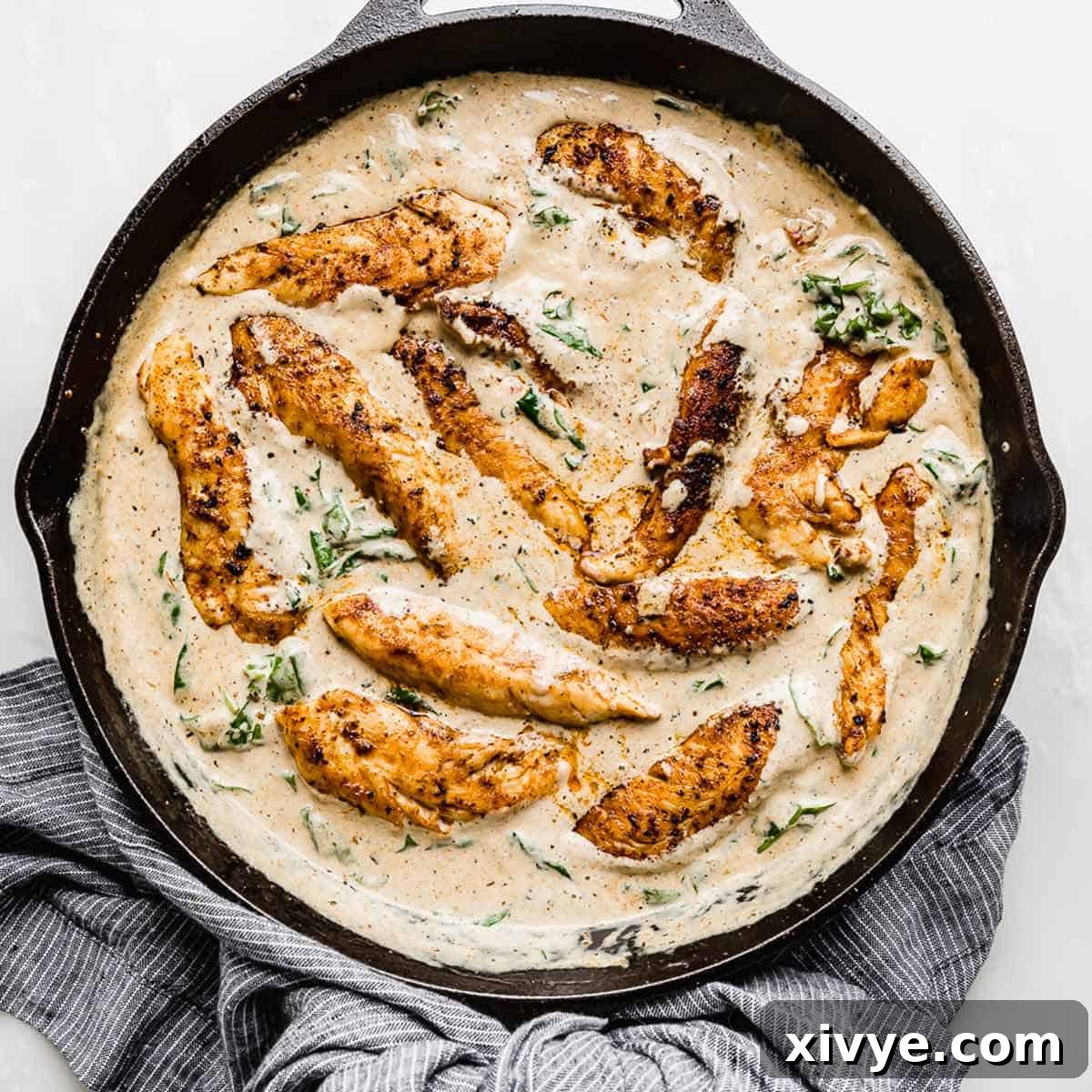 Succulent Creamy Tuscan Chicken simmering in a black skillet, with vibrant sun-dried tomatoes and fresh spinach leaves nestled within the rich, creamy sauce.