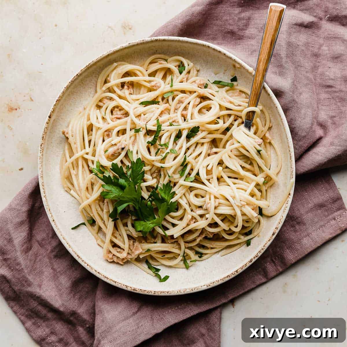 A generous serving of Tuna Carbonara beautifully arranged on a white plate, resting elegantly on a soft mauve napkin.