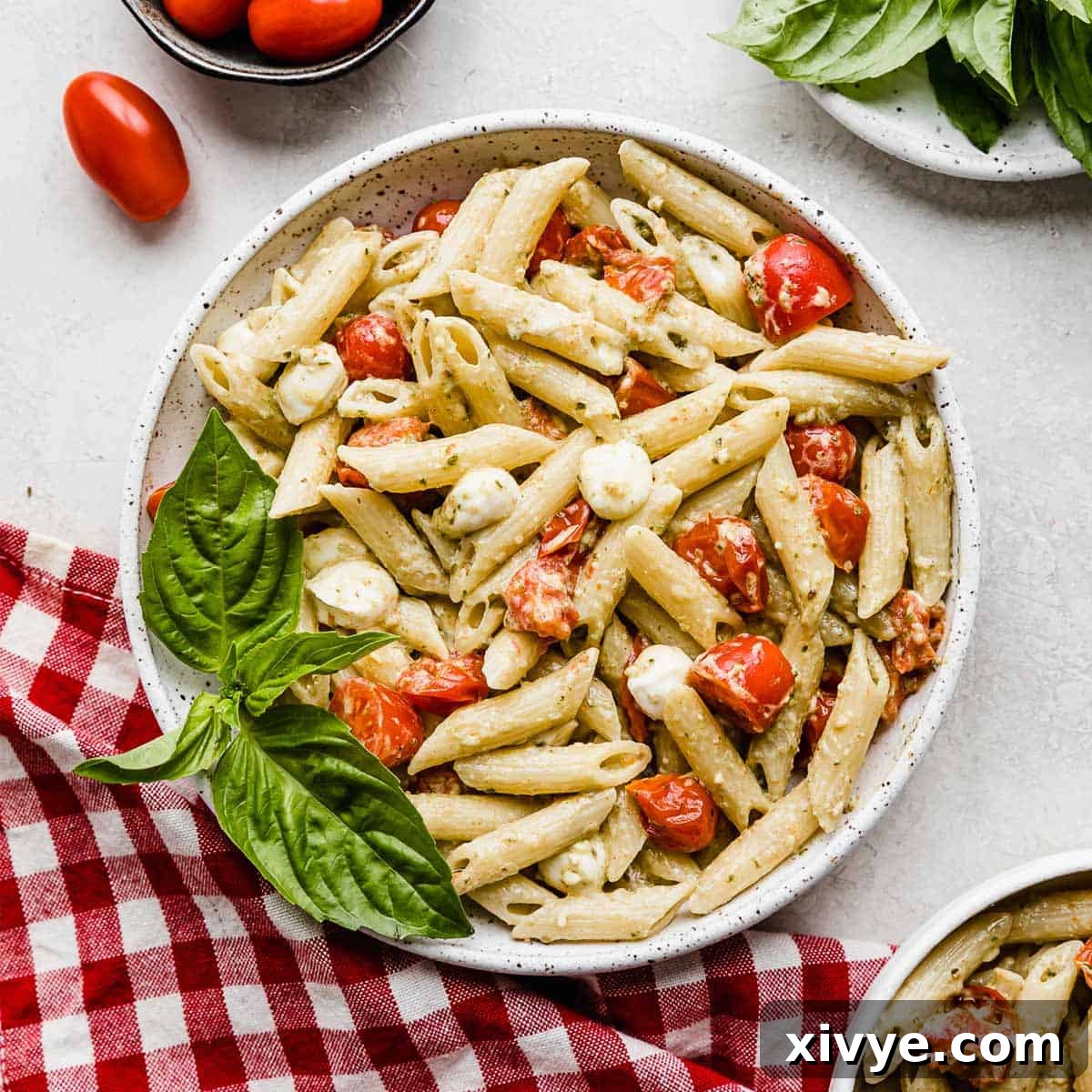 A large bowl of creamy pesto pasta, generously mixed with vibrant tomatoes and tender mozzarella balls, creating a feast for the eyes and palate.
