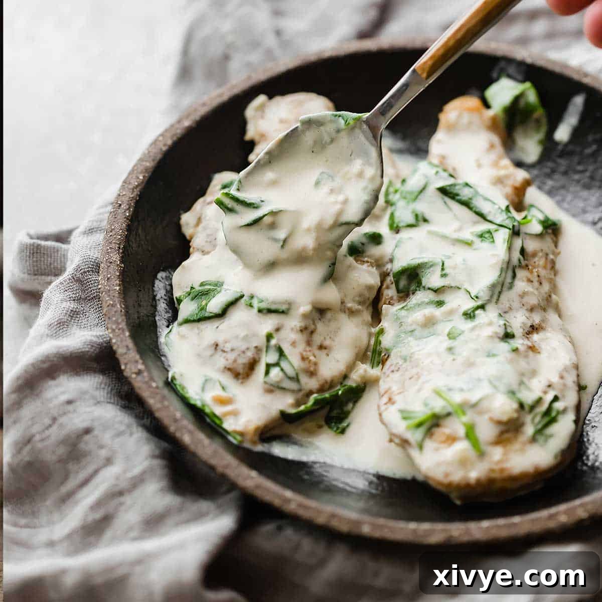A spoon delicately pouring creamy mustard sauce over a perfectly cooked Chicken Dijon breast, enhancing its rich appeal.