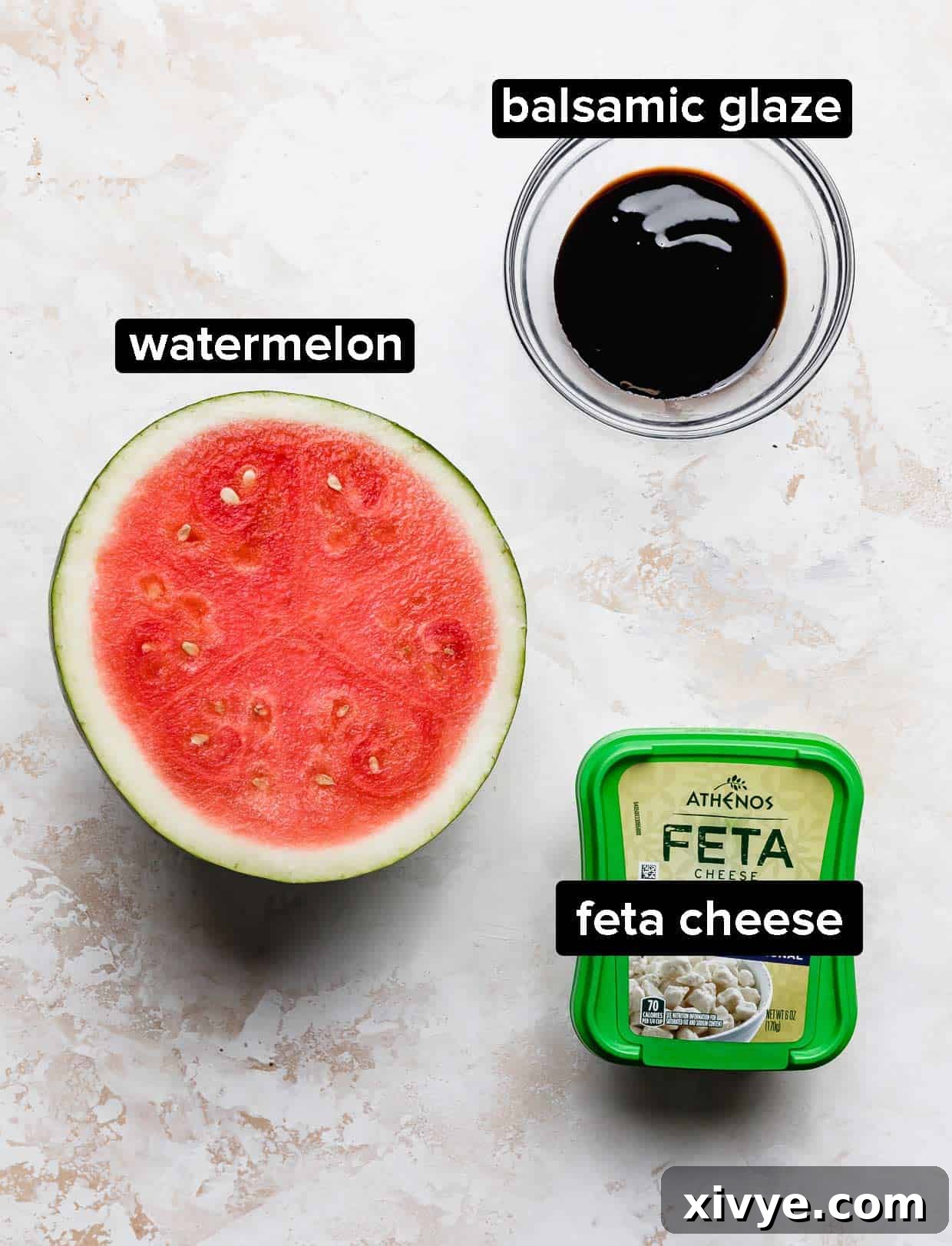 Watermelon Skewer ingredients: balsamic glaze, half a watermelon, and feta cheese on a white textured background.
