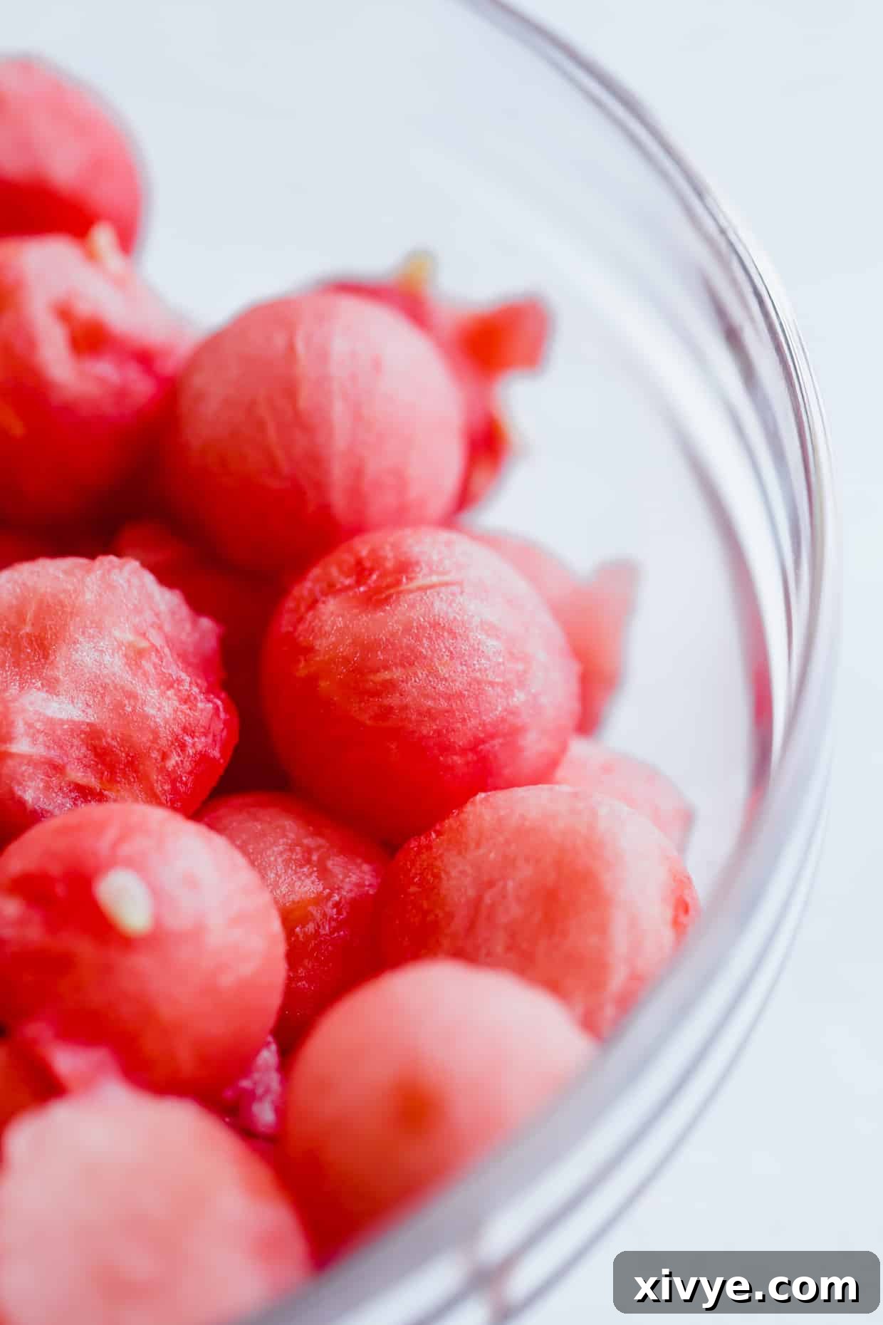 A close up photo of watermelon balls in a glass bowl.