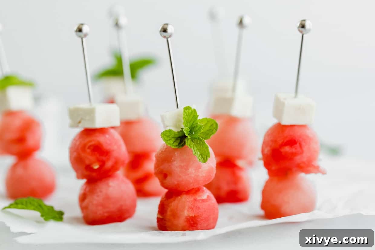 Two watermelon balls and small block of feta cheese on small metal skewers.