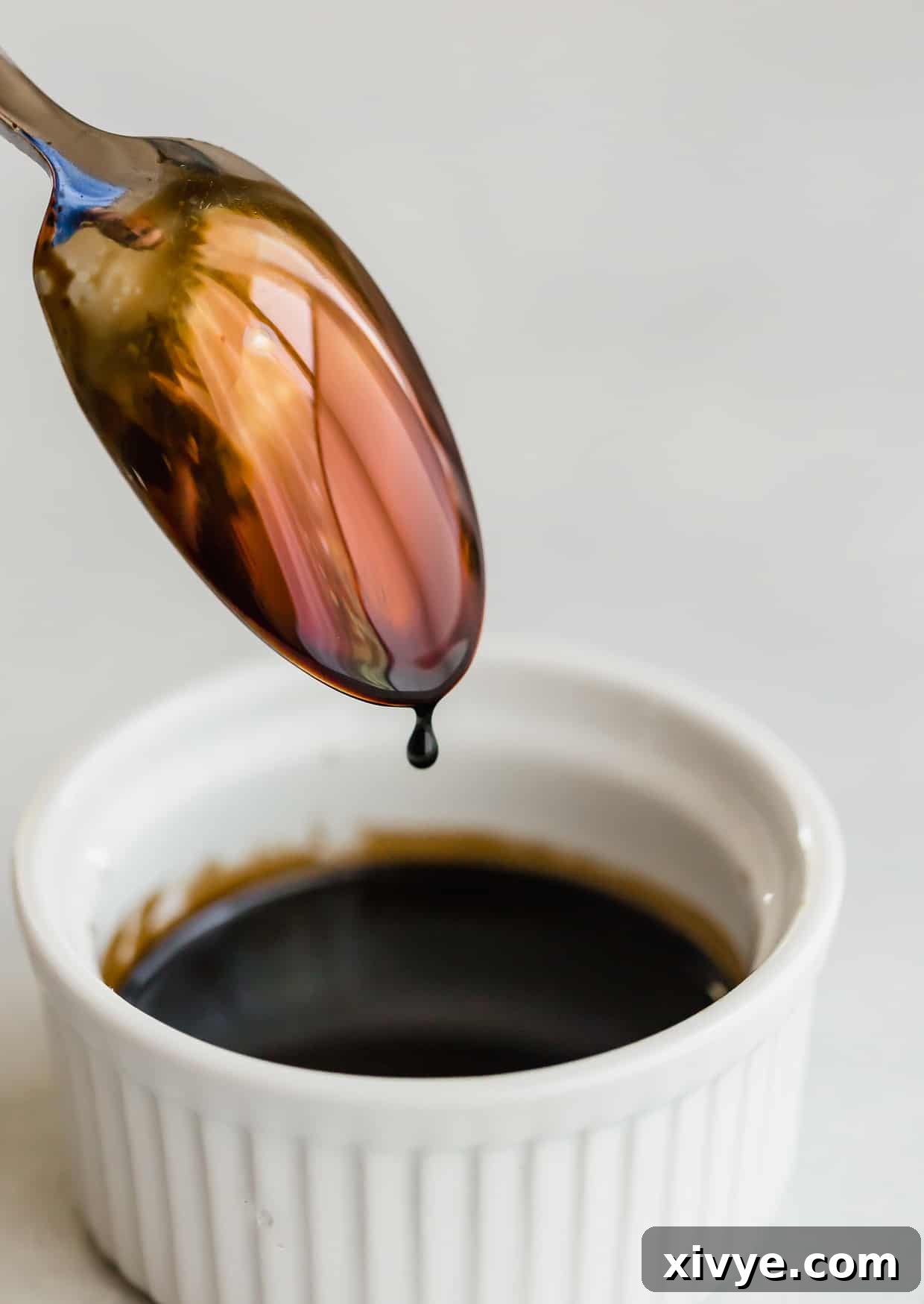 Balsamic reduction in a white bowl and a spoon just dipped into the sauce.