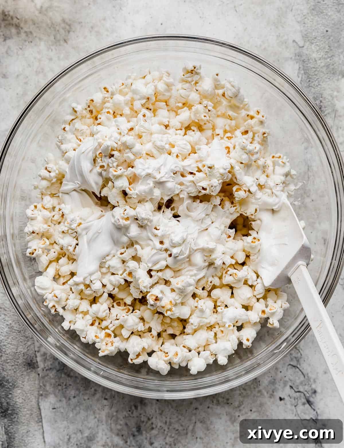Popcorn kernels being coated in melted white chocolate, showing the gooey texture.