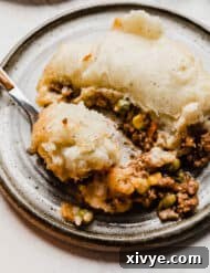 A perfectly portioned slice of Shepherd's Pie, garnished with fresh rosemary, showing off the vibrant corn and peas embedded in the savory ground beef mixture.