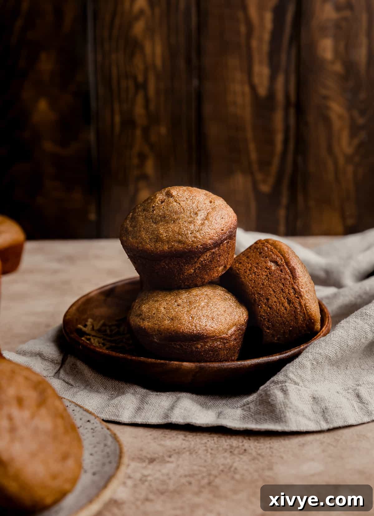 Hearty Buttermilk Bran Muffins 2 All Bran Muffins with buttermilk stacked on a small wooden plate against a wooden background.