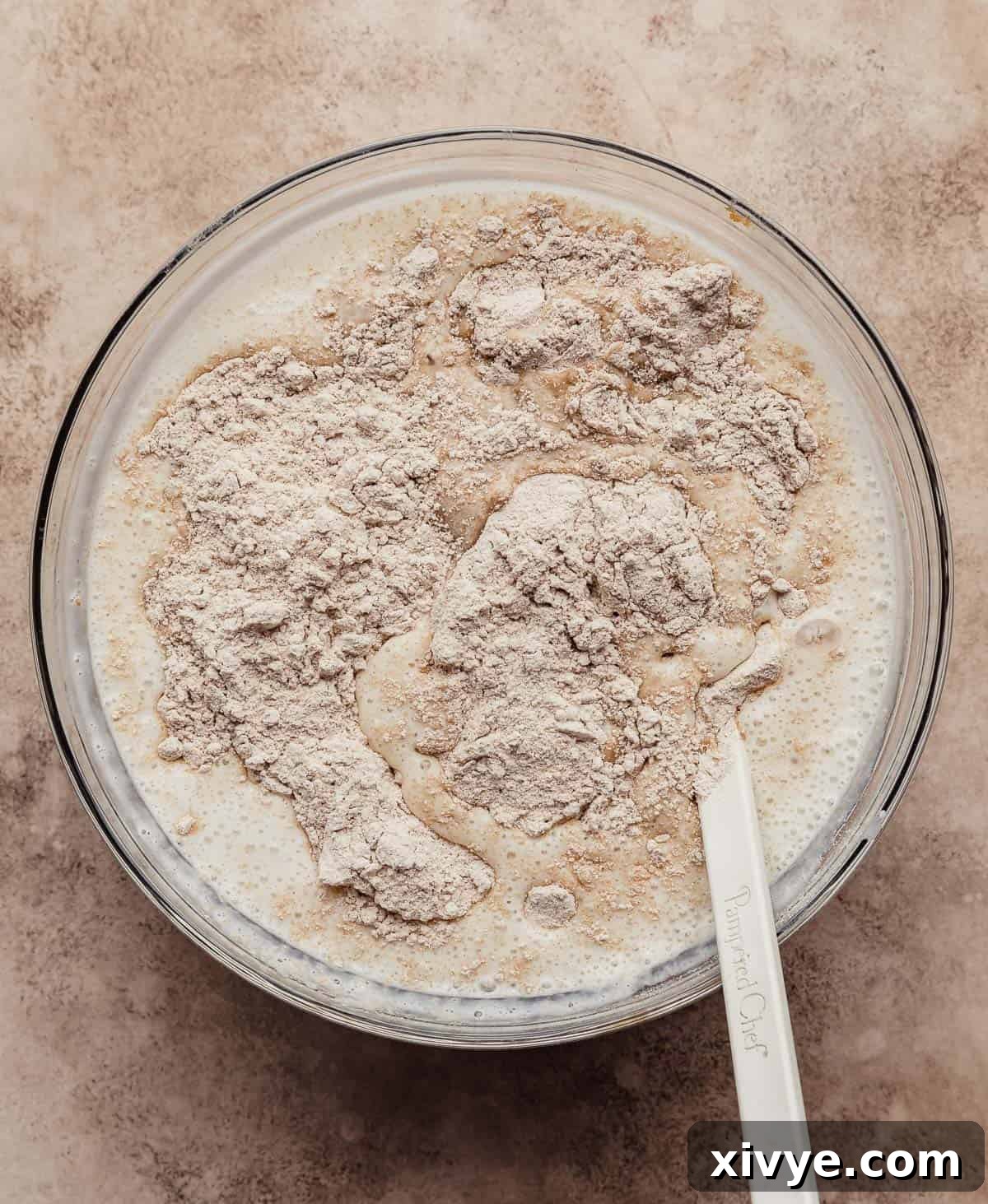 Hearty Buttermilk Bran Muffins 9 Whole wheat flour in a glass bowl on a light brown textured background.