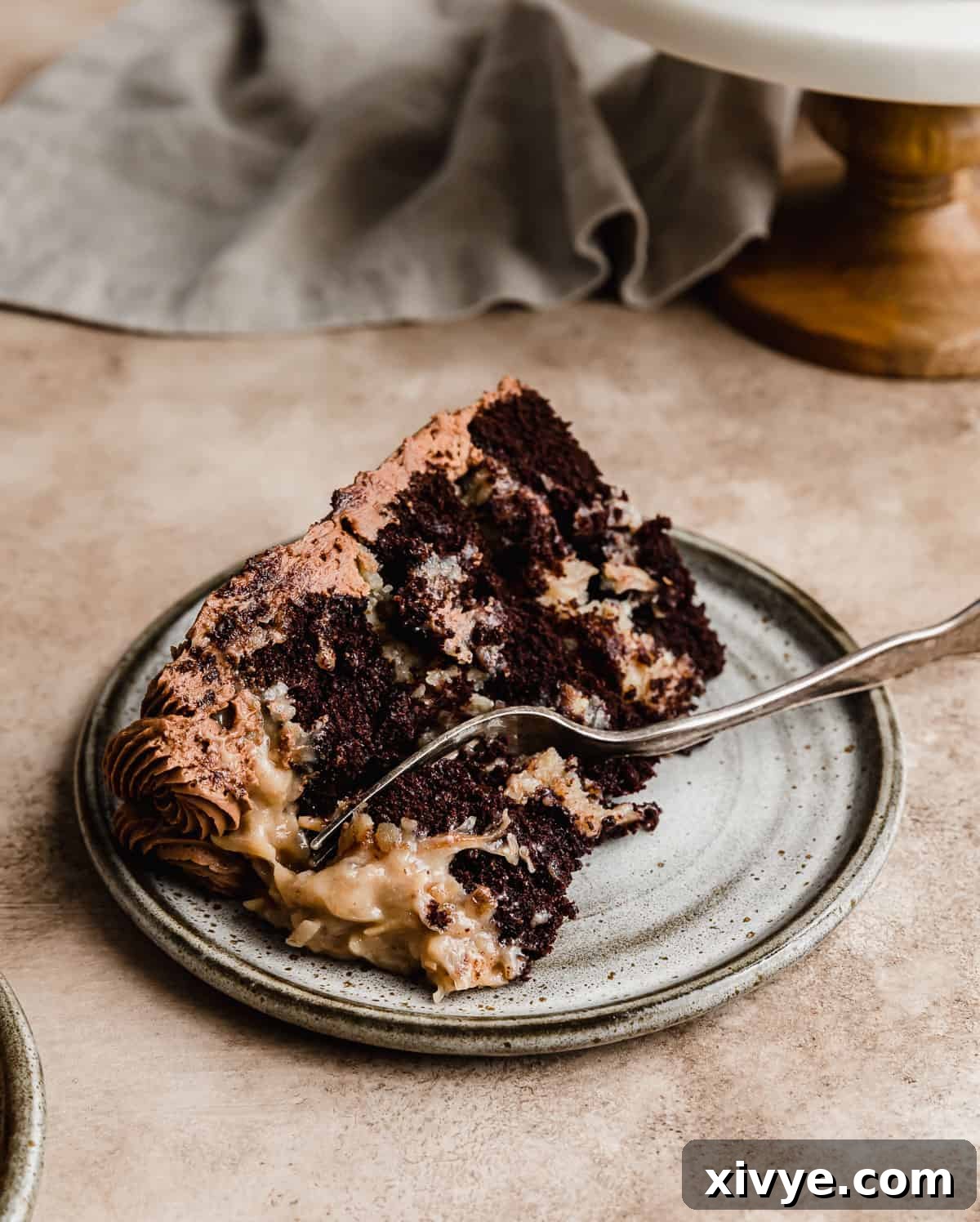 A perfectly sliced Small German Chocolate Cake on a elegant gray plate, revealing its moist layers and rich coconut pecan frosting, with a fork gently cutting into the cake.