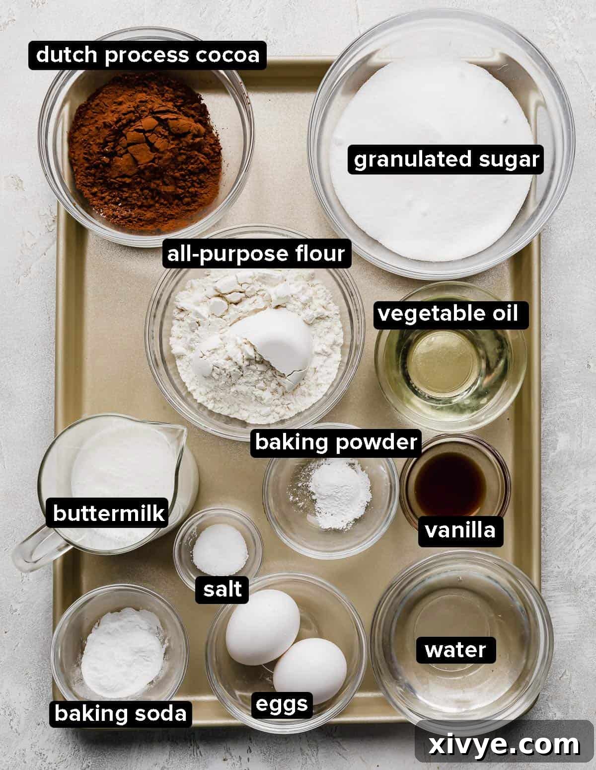 A curated display of Small German Chocolate Cake ingredients, beautifully arranged in clear glass bowls on a rustic bronze baking sheet.