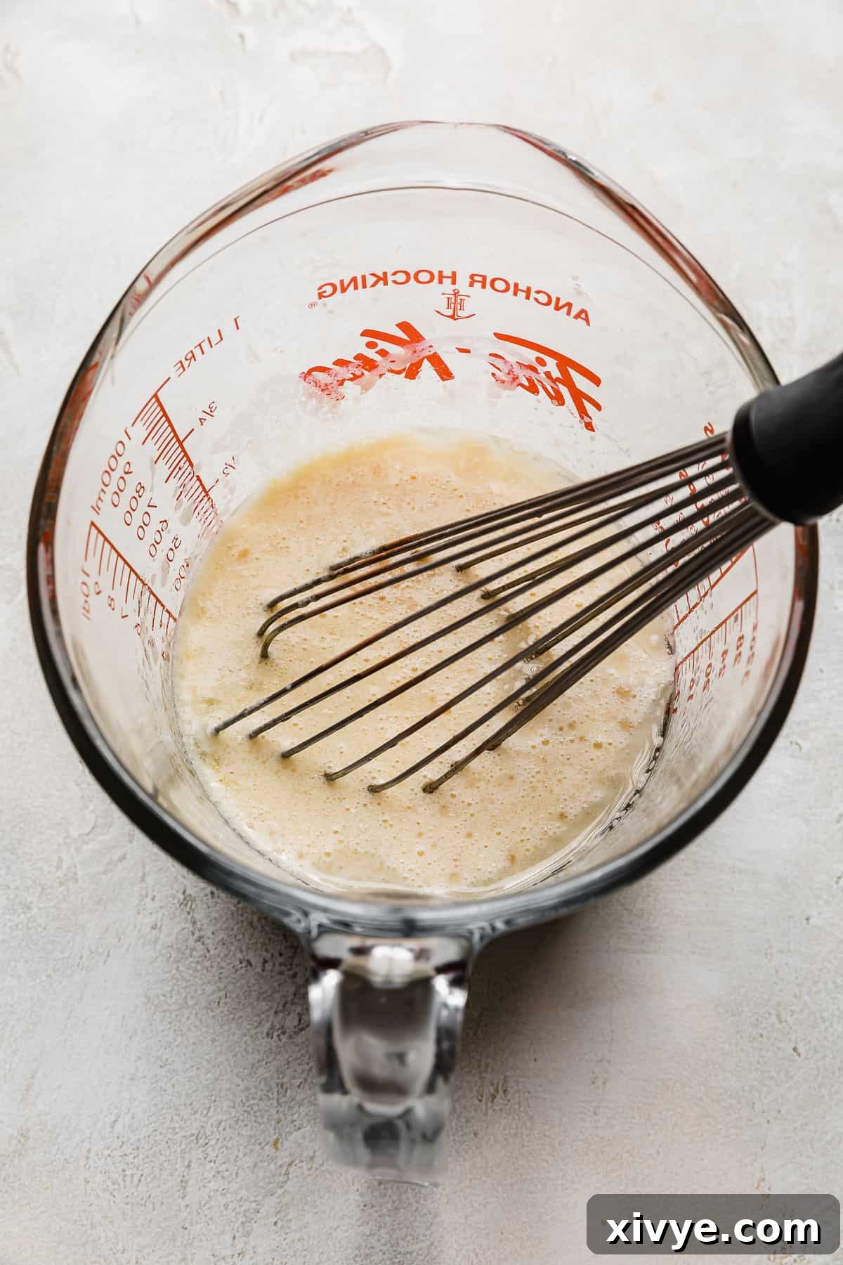 A light yellow liquid mixture, composed of egg, buttermilk, oil, and vanilla, in a clear liquid measuring cup, ready to be added to the dry ingredients for a 6 inch German Chocolate Cake.
