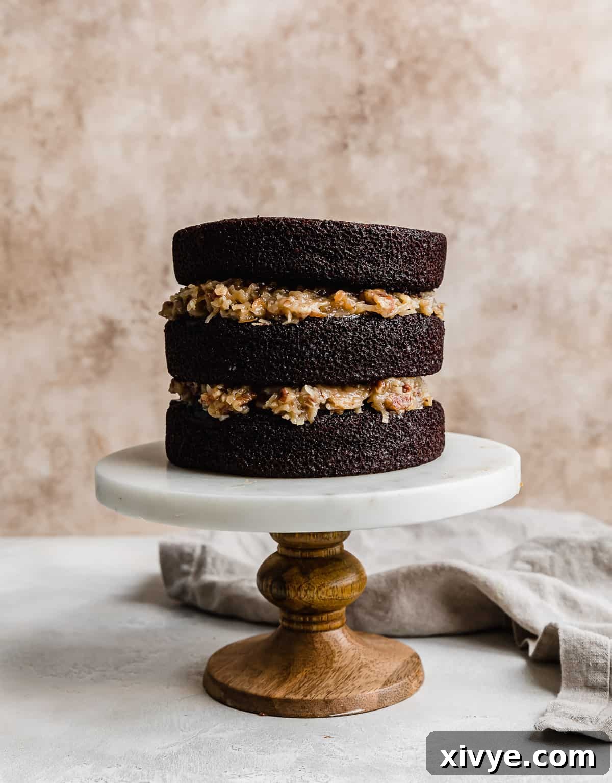 A three-tier German chocolate cake showing off its generous layers of moist chocolate cake separated by abundant, irresistible coconut pecan frosting.