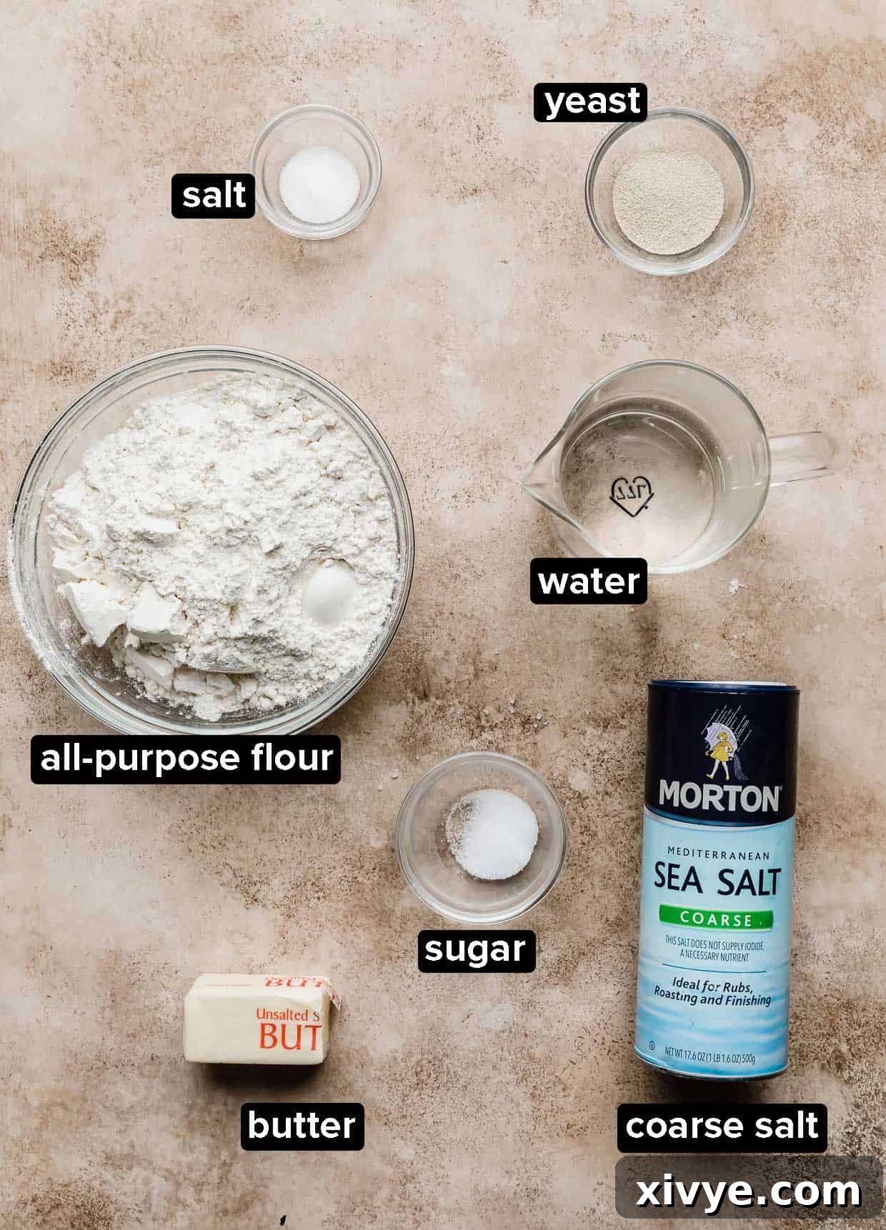 Pillowy Homemade Soft Pretzels 3 Homemade Soft Pretzels ingredients on a textured light brown background.