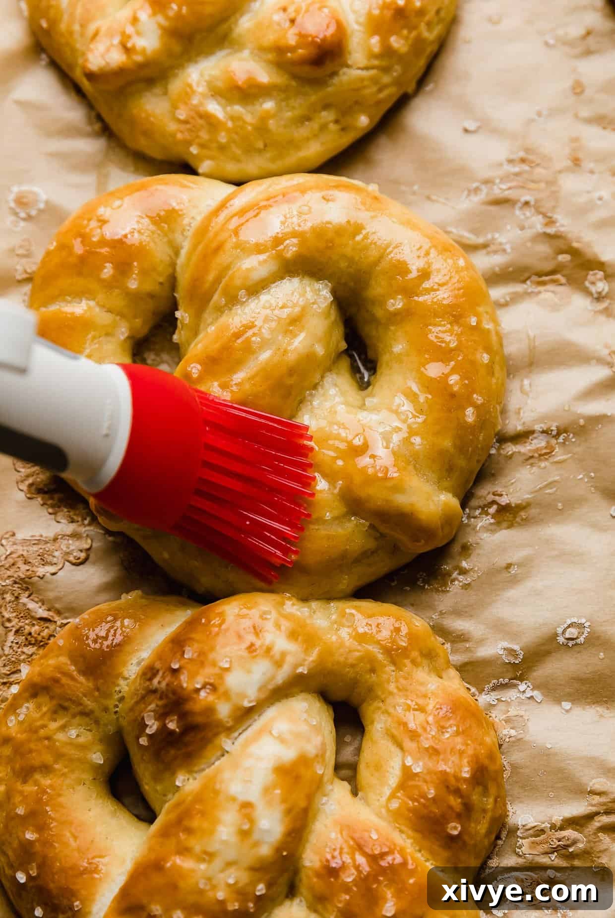 Pillowy Homemade Soft Pretzels 9 A red pastry brush spreading melted butter over a golden baked pretzel.