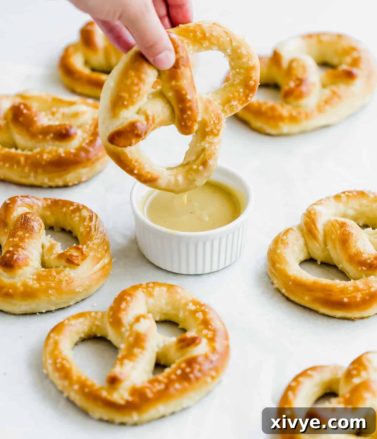 Pillowy Homemade Soft Pretzels 10 A golden brown pretzel sprinkled with coarse salt being dipped into a small bowl of honey mustard sauce.