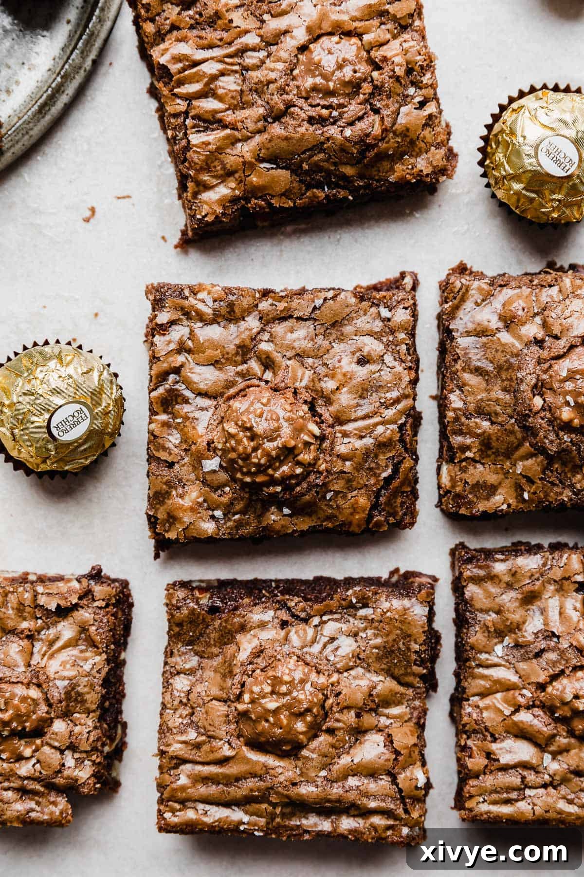 Ferrero Rocher Brownies topped with an unwrapped Ferrero Rocher candy, on a white background.