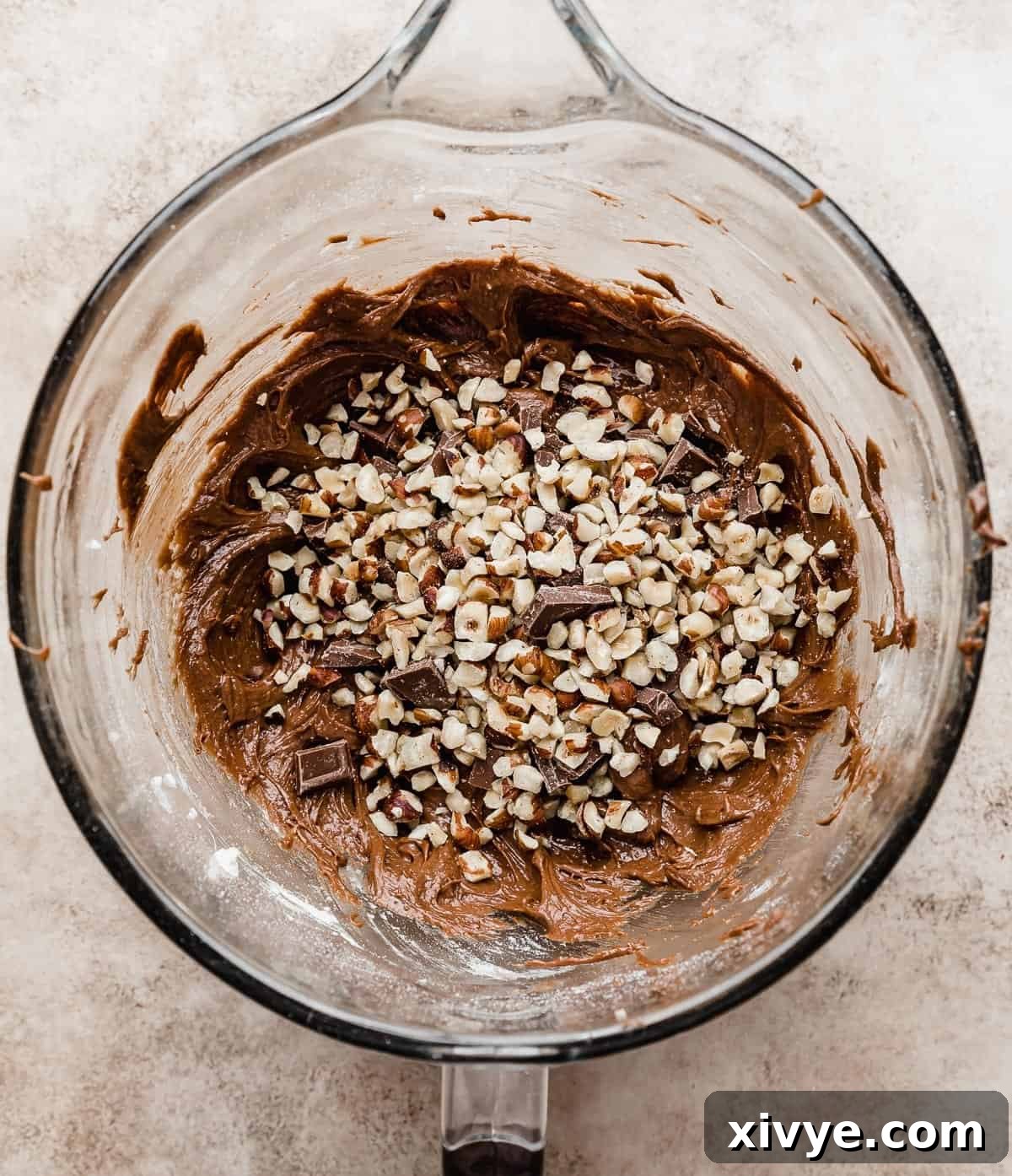 Chopped hazelnuts overtop a Nutella brownie batter in a glass bowl.