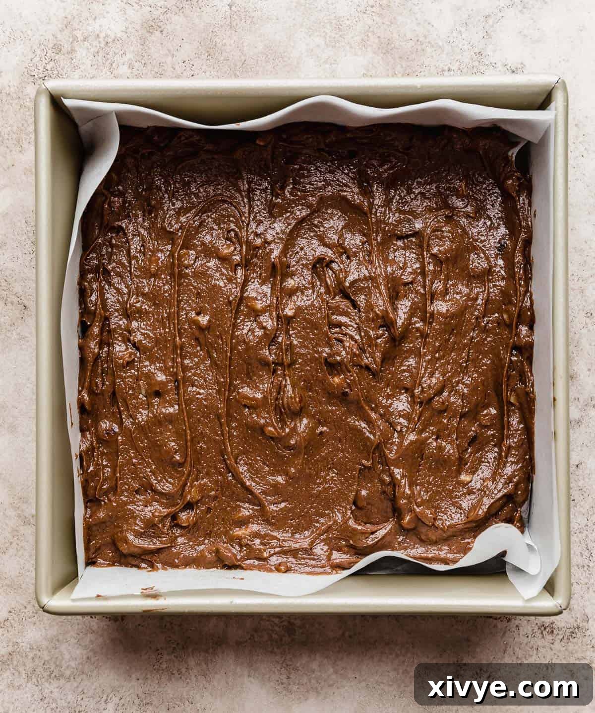 Dark brown brownie batter with Ferrero Rocher's in a square baking pan.