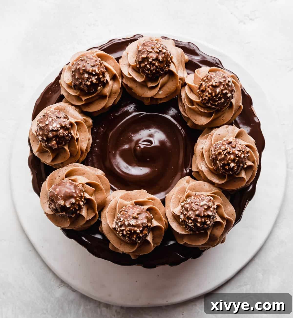 Ultimate Ferrero Rocher Indulgence 8 An overhead photo of a Ferrero Rocher Cake that's topped with a chocolate ganache and swirls of chocolate frosting garnished with unwrapped Ferrero Rocher candies.