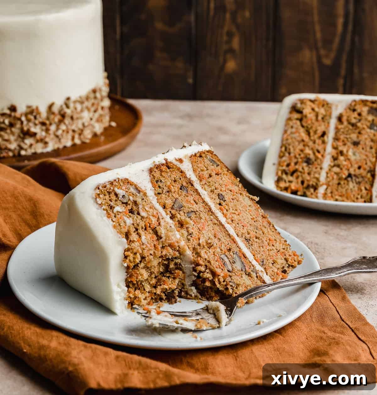 Sunshine Pineapple Pecan Carrot Cake 11 A slice of a three layered carrot cake on a white plate on a burnt orange napkin.