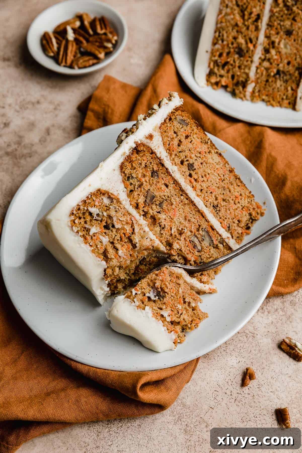 Sunshine Pineapple Pecan Carrot Cake 3 A slice of carrot cake with pecans and pineapple, frosted with white frosting on a white plate.