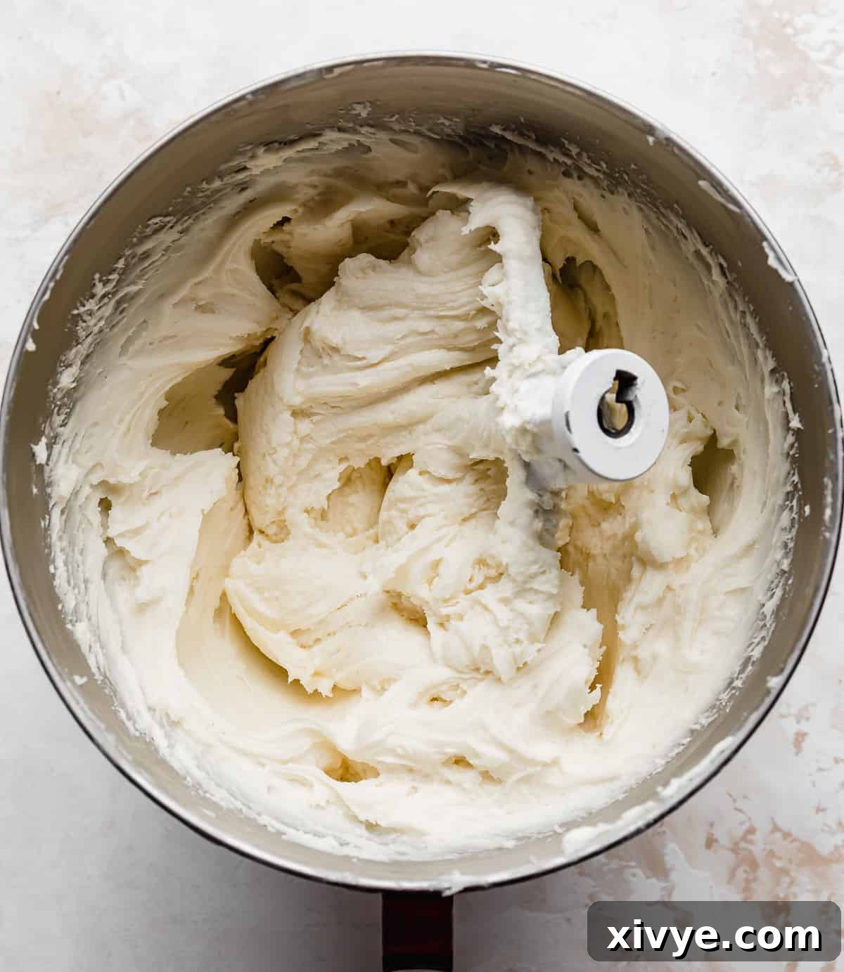 Sunshine Pineapple Pecan Carrot Cake 4 A metal bowl filled with white cream cheese frosting against a white background.